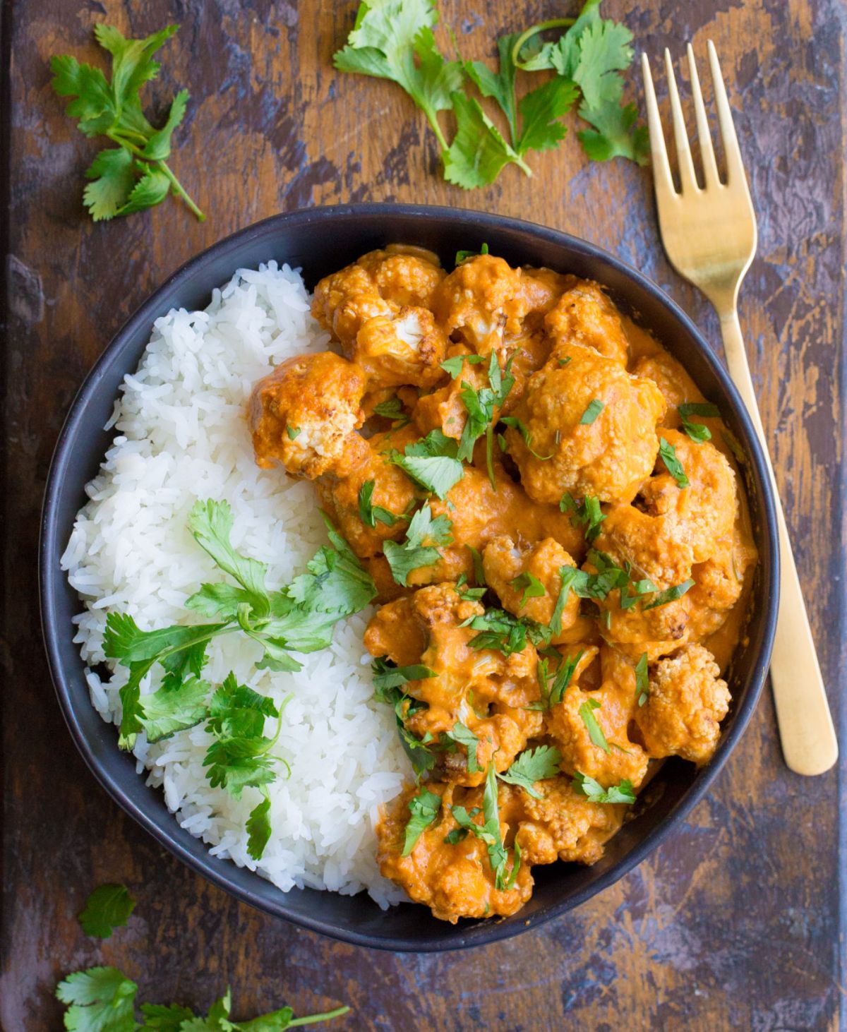 A black owl of cualiflower curry with rice and cilantro sprinkled on top