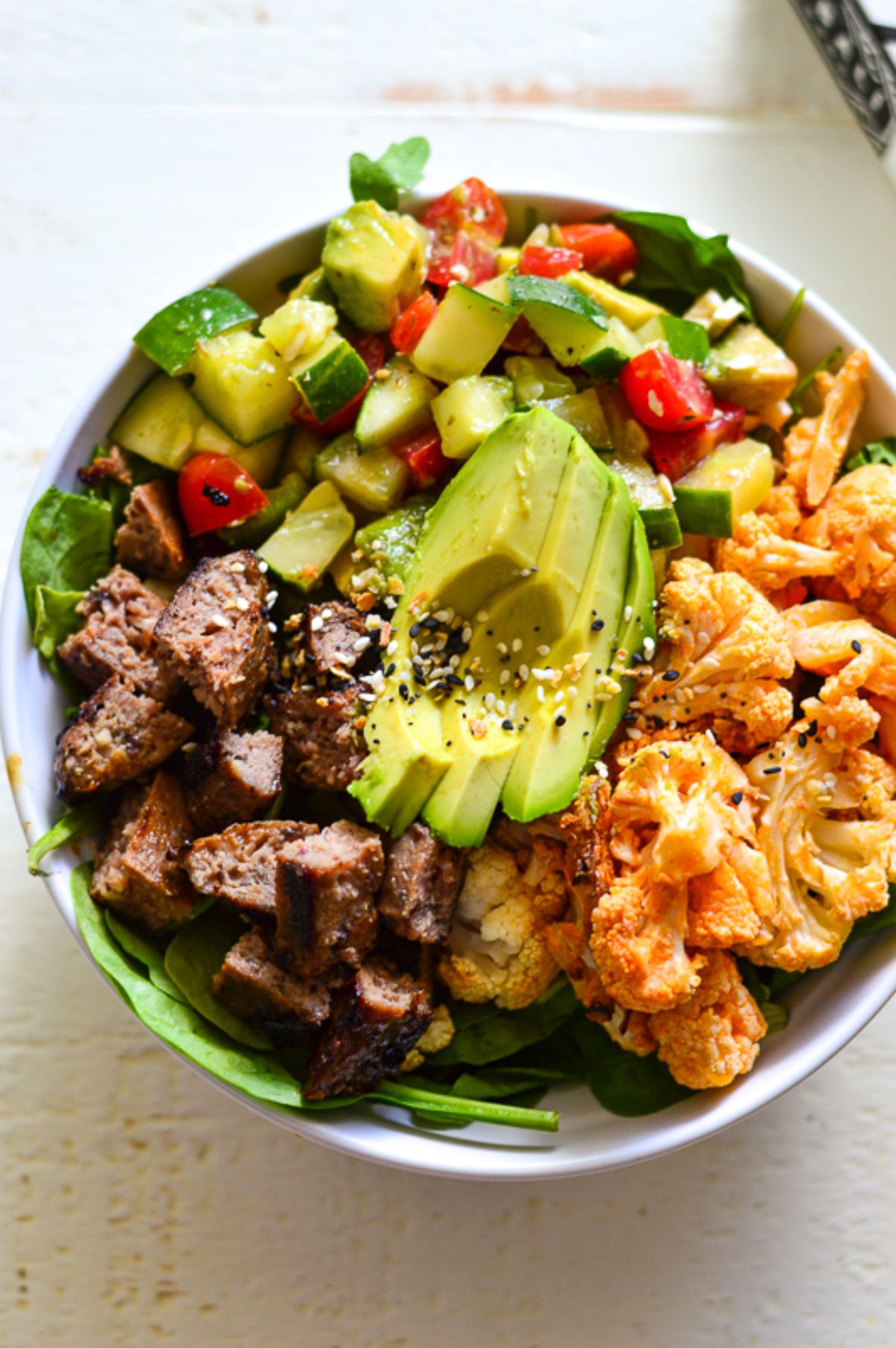 A white bowl of cauliflower, avocado, red meat and chopped salsa