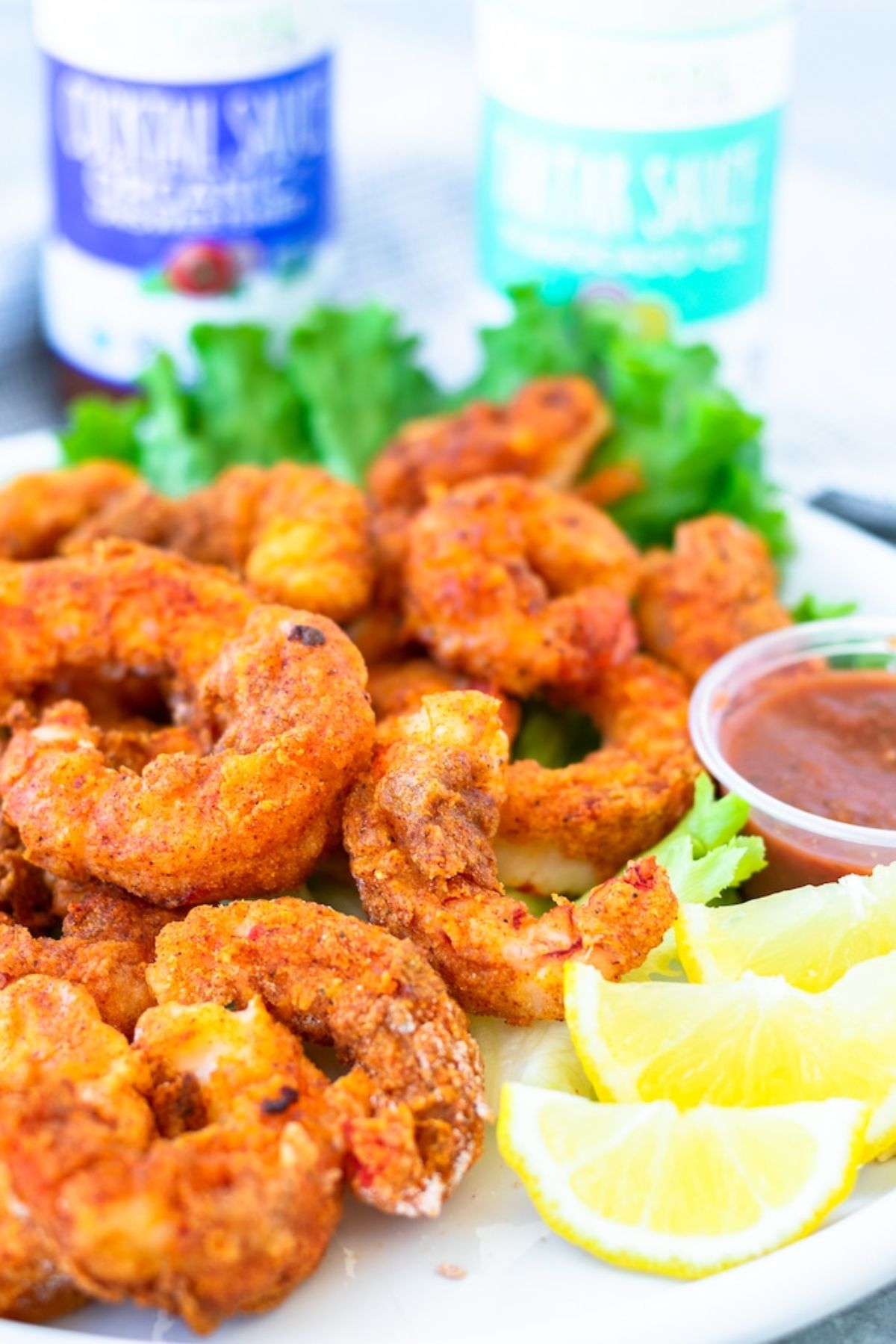 a plate of popcorn shrimp, lettuce leaves, sliced lemons and dip