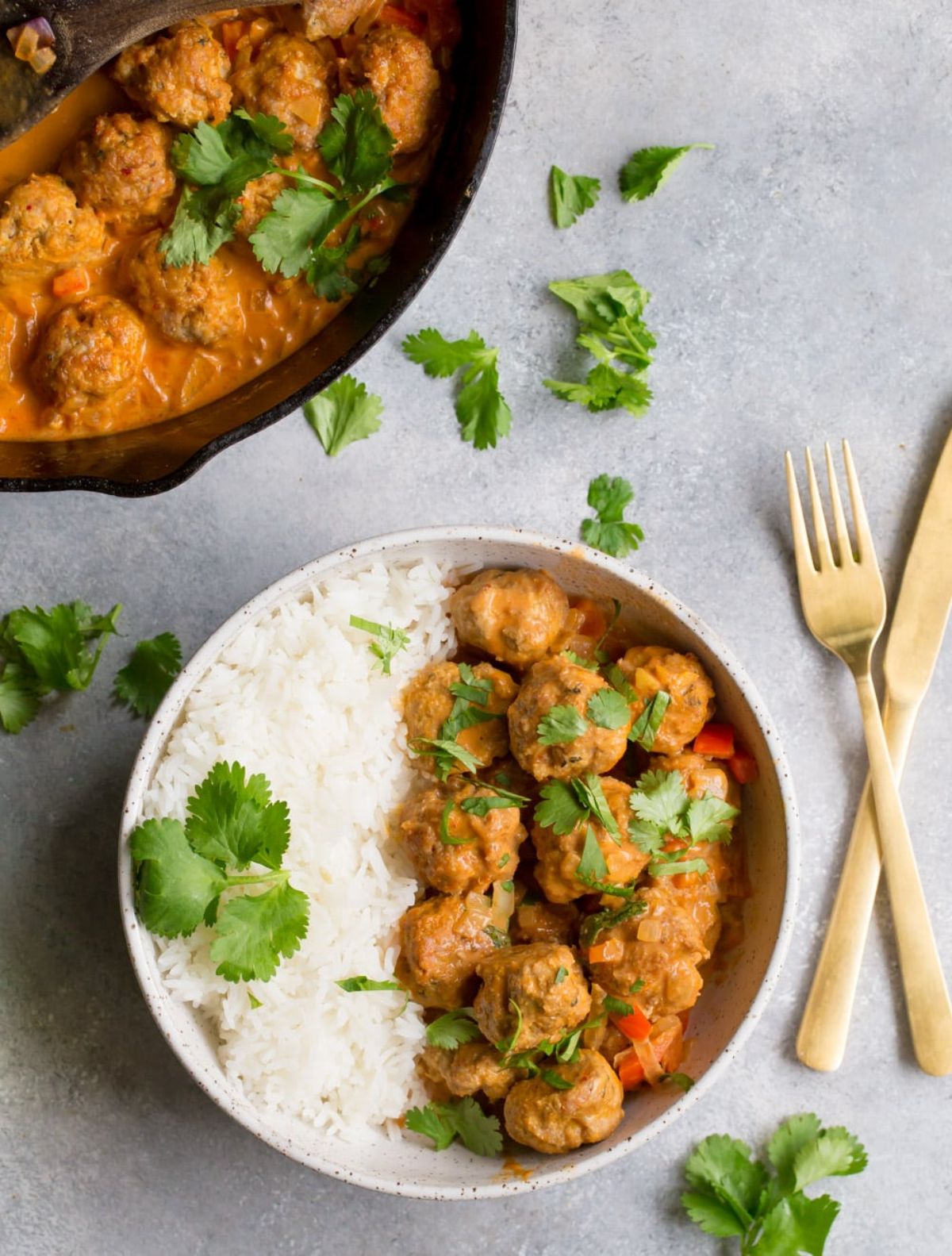 A white bowl of meatblass and rice, with a golden set of cutlery next to it and cilantro scattered around