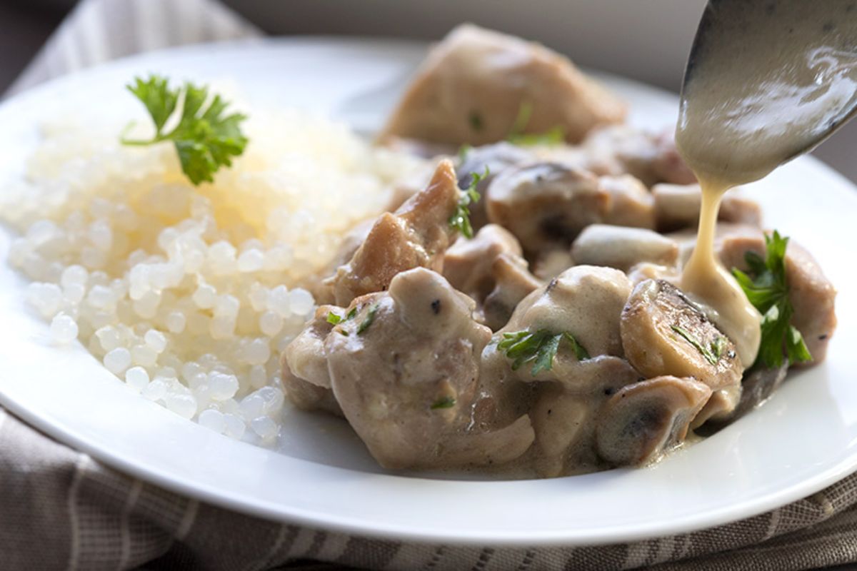 A white wide soup dish is mid shot with chicken and mushrroms in it, and a spoon to the top right