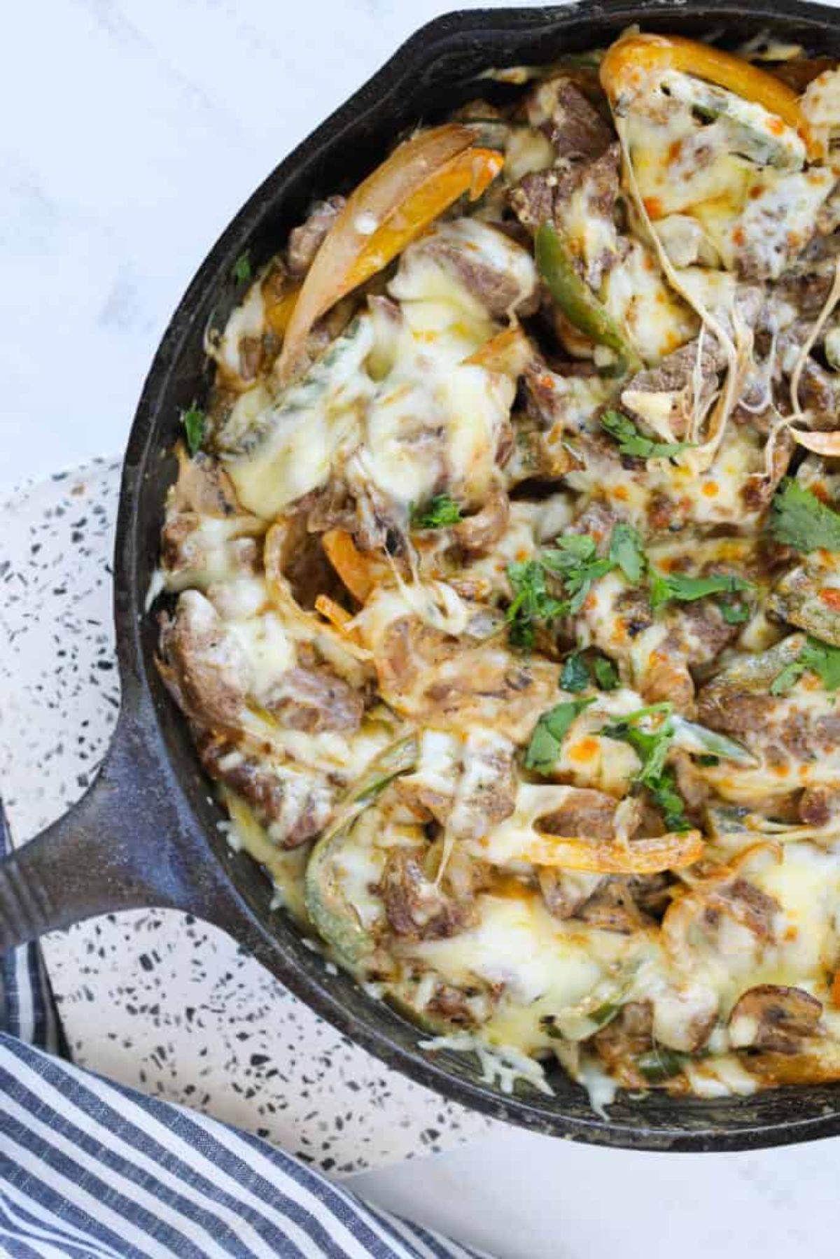 A section of a cast iron skillet, containing a cheesy casserole with green garnish