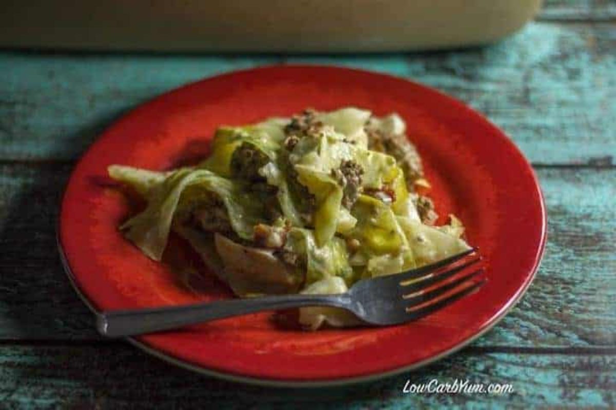 On a red plate is a portion of a cheesy casserole and a metal fork