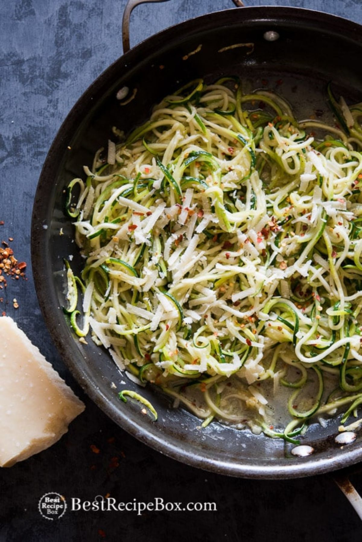 On a blue surface is a wok filled with Zucchini noodles