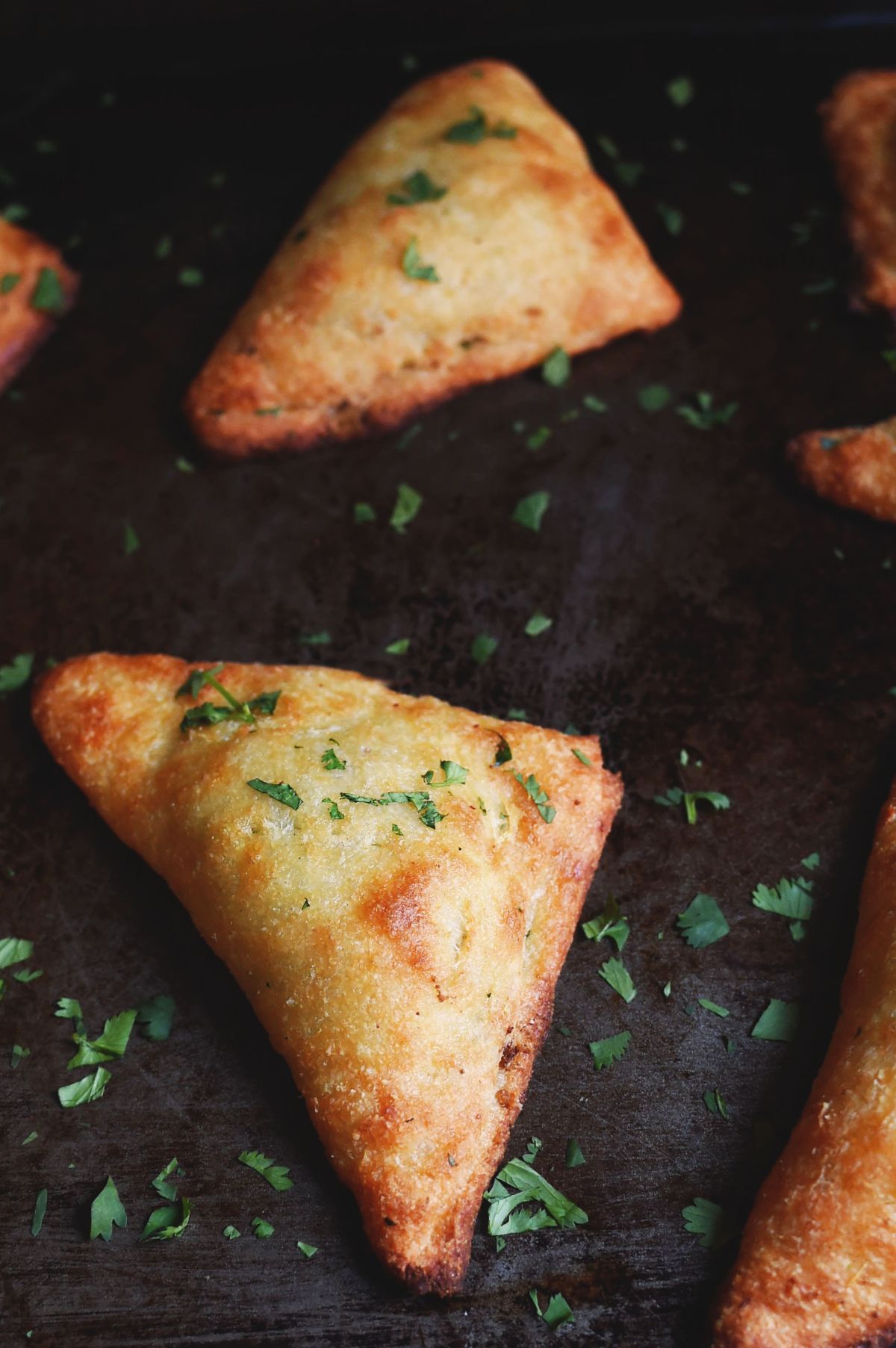 A partial shot of a skillet with 2 vegetable samosas sprinkled with chopped herbs