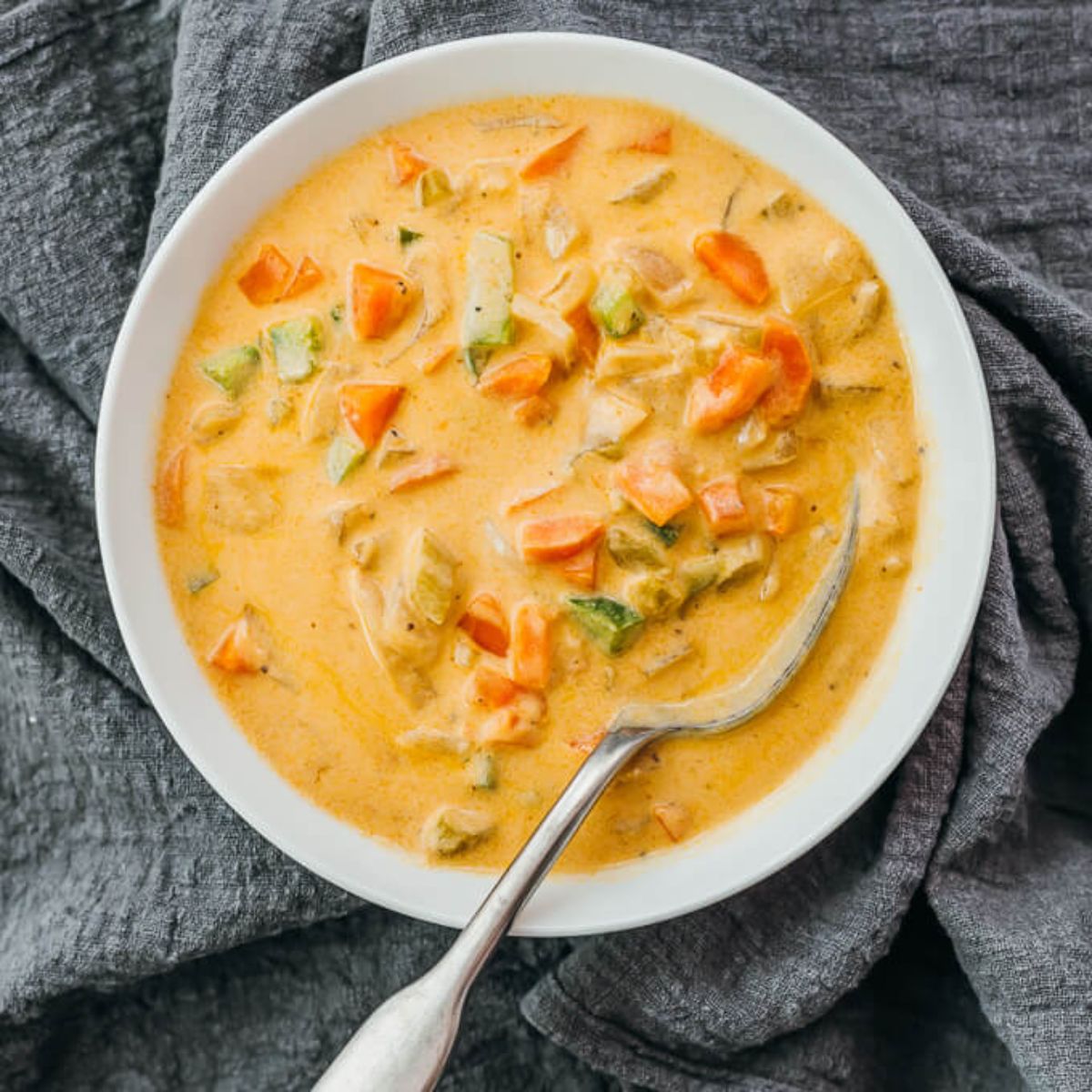 A gray cloth is underneath a round white bowl filled with vegetables in a creamy tomato sauce