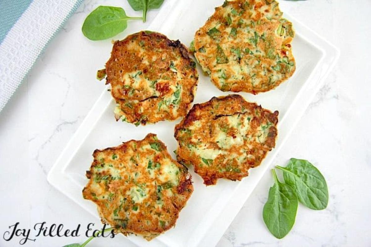 On a white countertop is a white rectangular dish with 4 spinach and feta pancakes on it. Basil leaves are scattered around