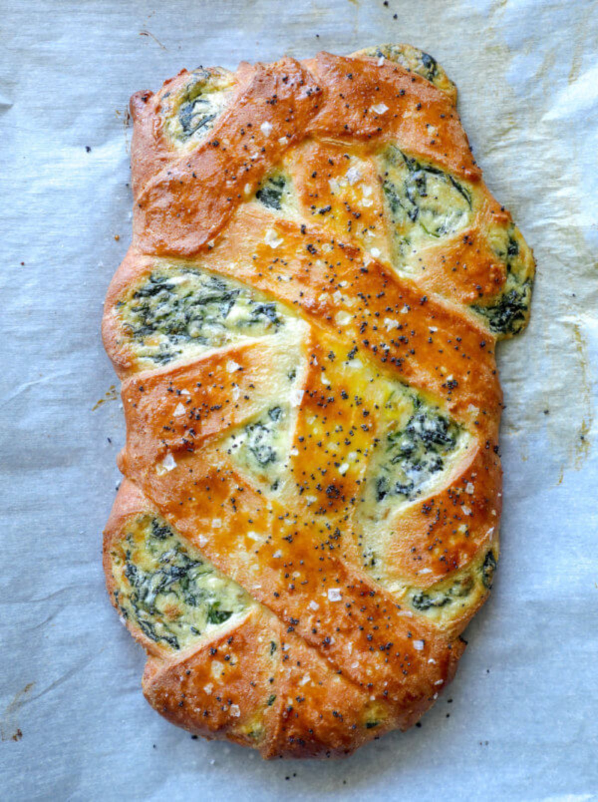 On a sheet of baking parchment is a calzone with spinach sneaking thorugh the layers.