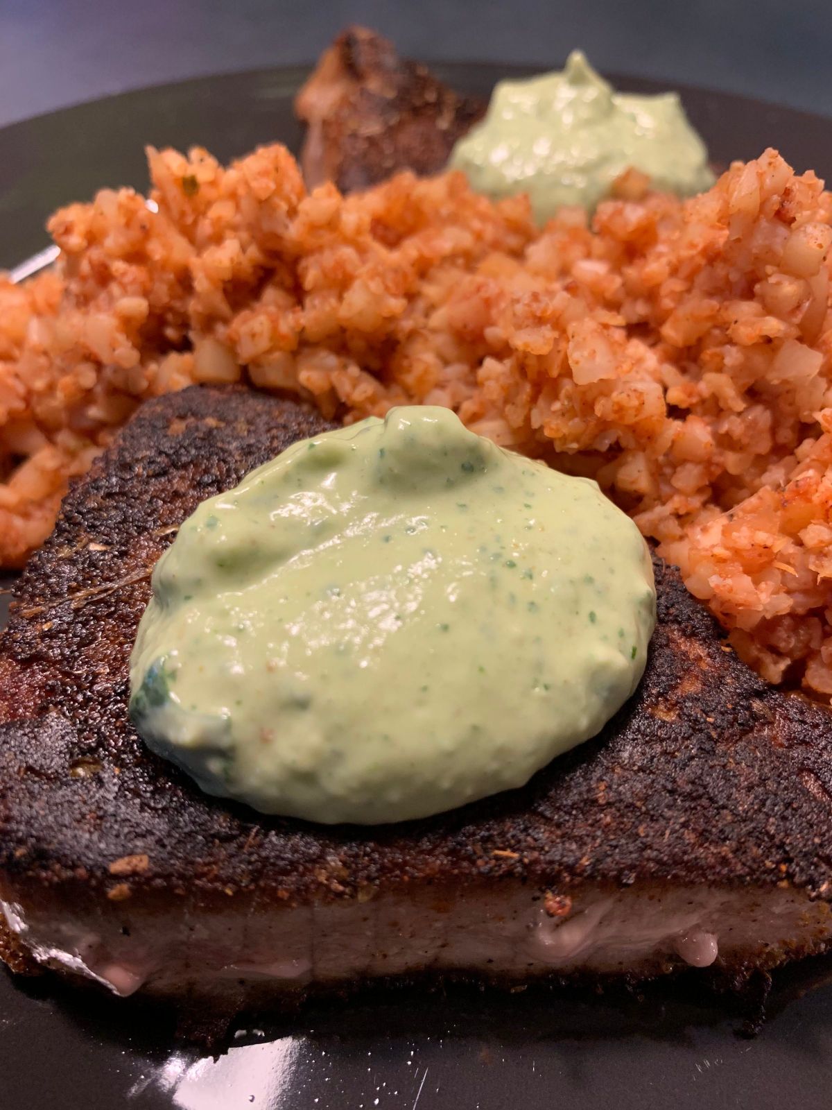 A partial shot of a dark gray plate with tomato cauliflower rice, seared tuna and a creamy sauce on top