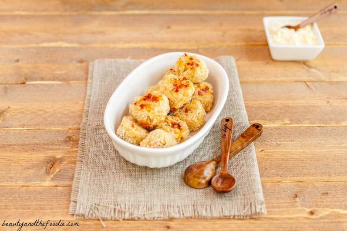 A light wooden table with a hessian rectangle in the middle. On this is a white oval casserole dish filled with tuna bites. To the right are two wooden spoons and just behind is a small square dish with sauce