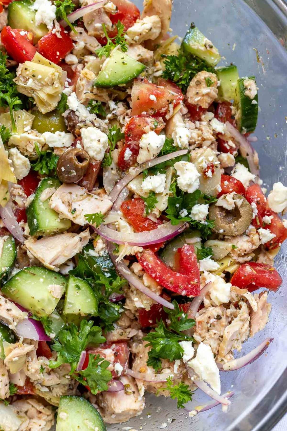 A partial shot of a silver bowl filled with a cucumber, tuna, tomato and red onion salad