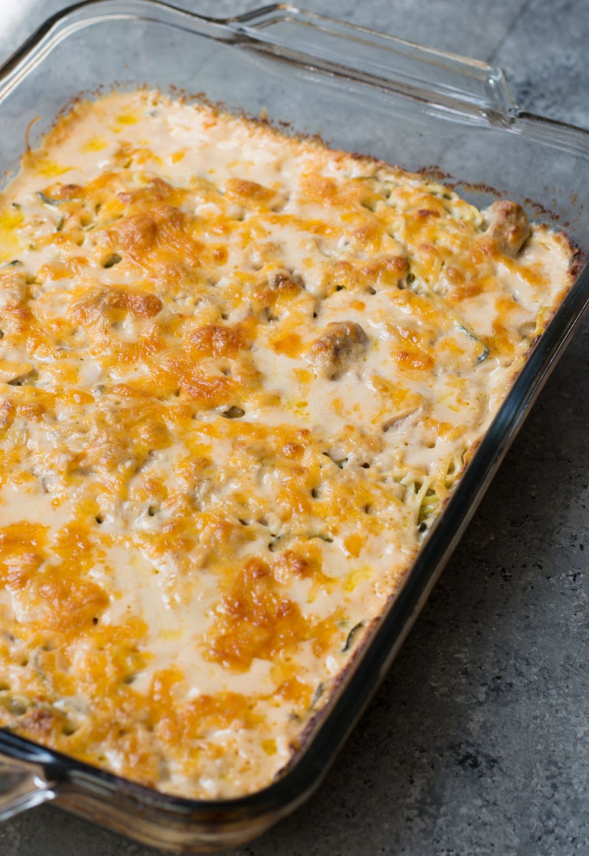 On a gray surface is a rectangular casserole dish filled with cheese-topped casserole