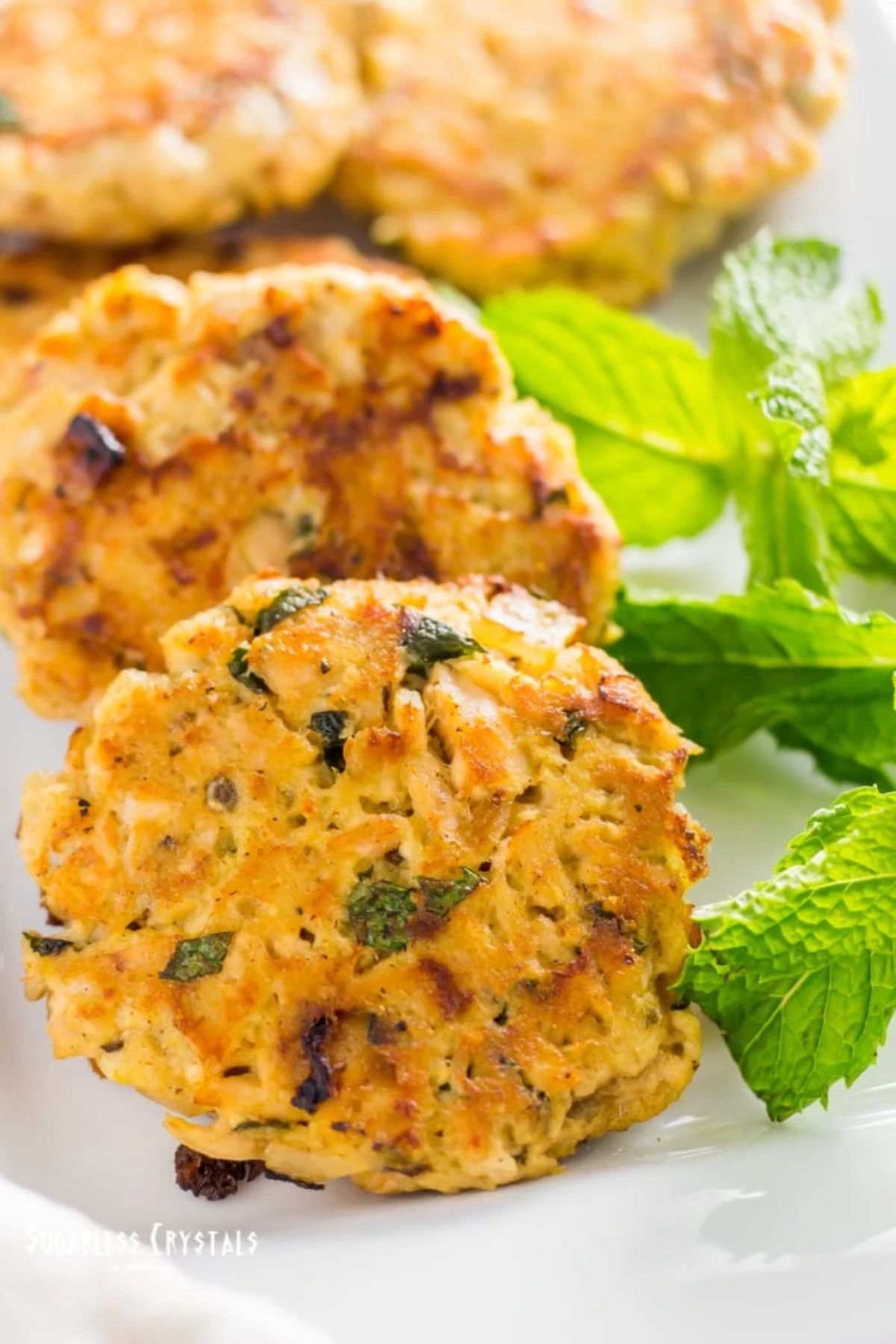 A partial shot of a white plate holding tuna cakes, with a sprig of mint on the right