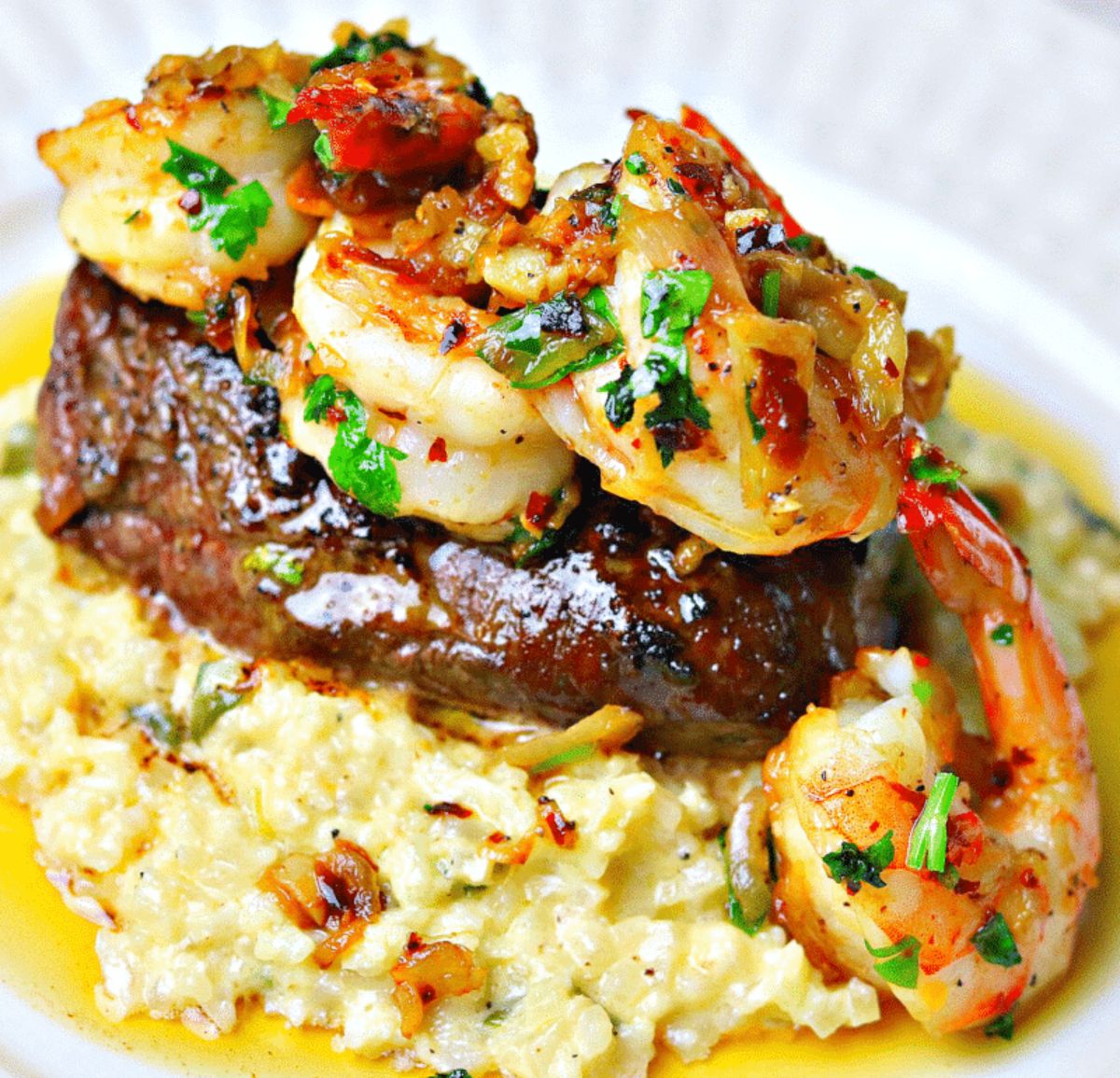 A close up of a pile of rice, steak and shrimp topped with a chilli and herb sauce