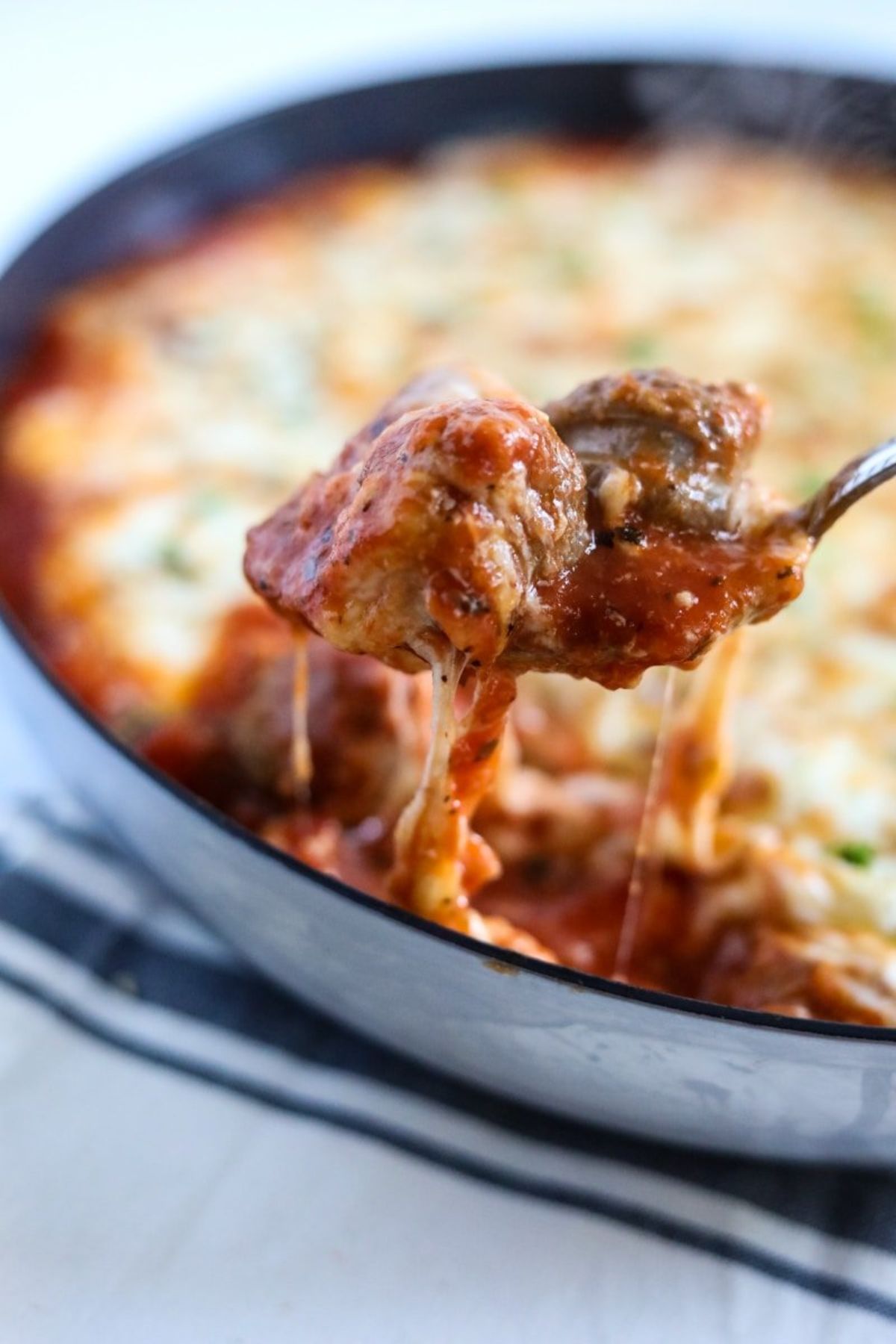 a blurred shot of bowl of casserole. A metal spoon is lifting a mouthful of cheese-coverd meat out of the bowl