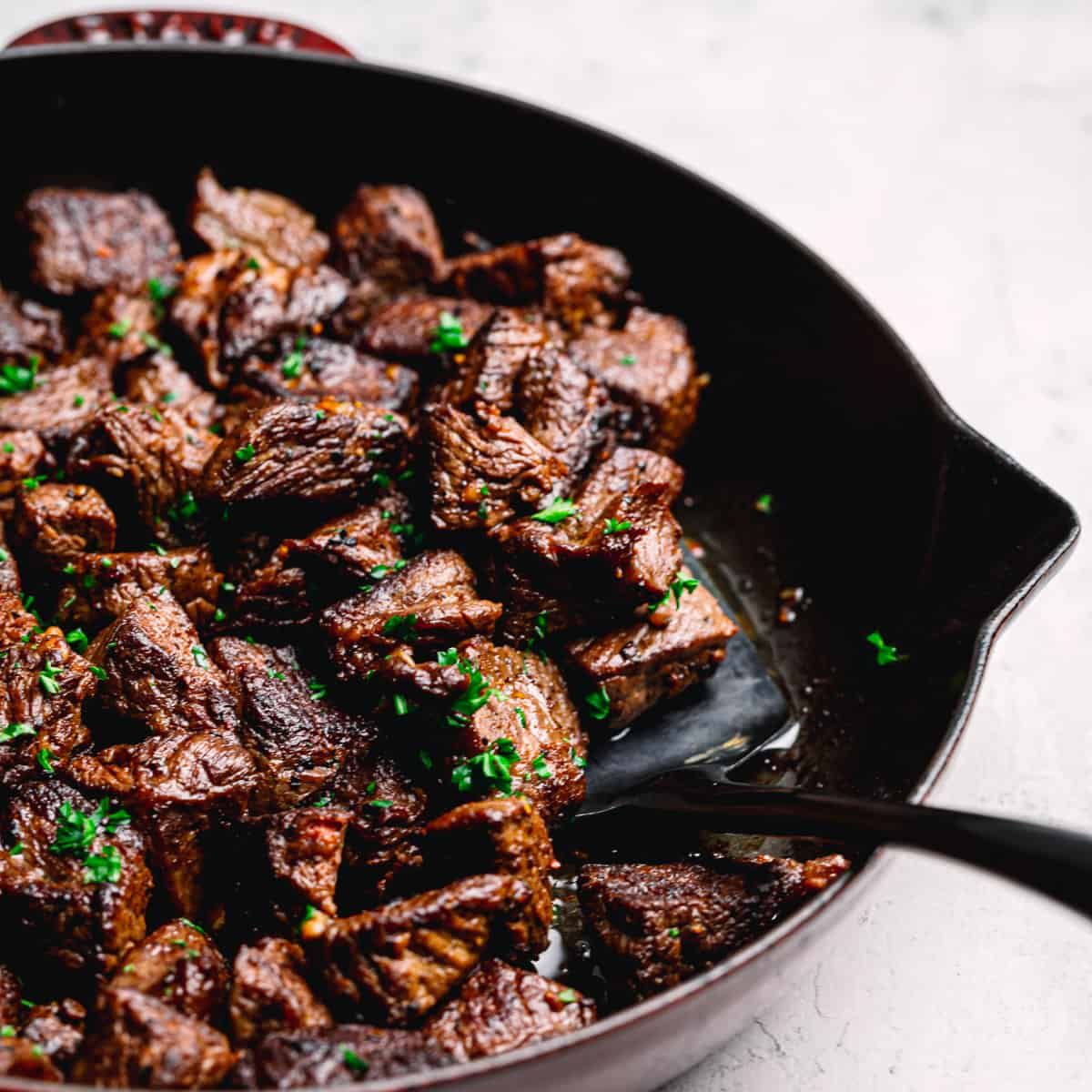 A partial shot of a skillet filled with steak bites and herbs