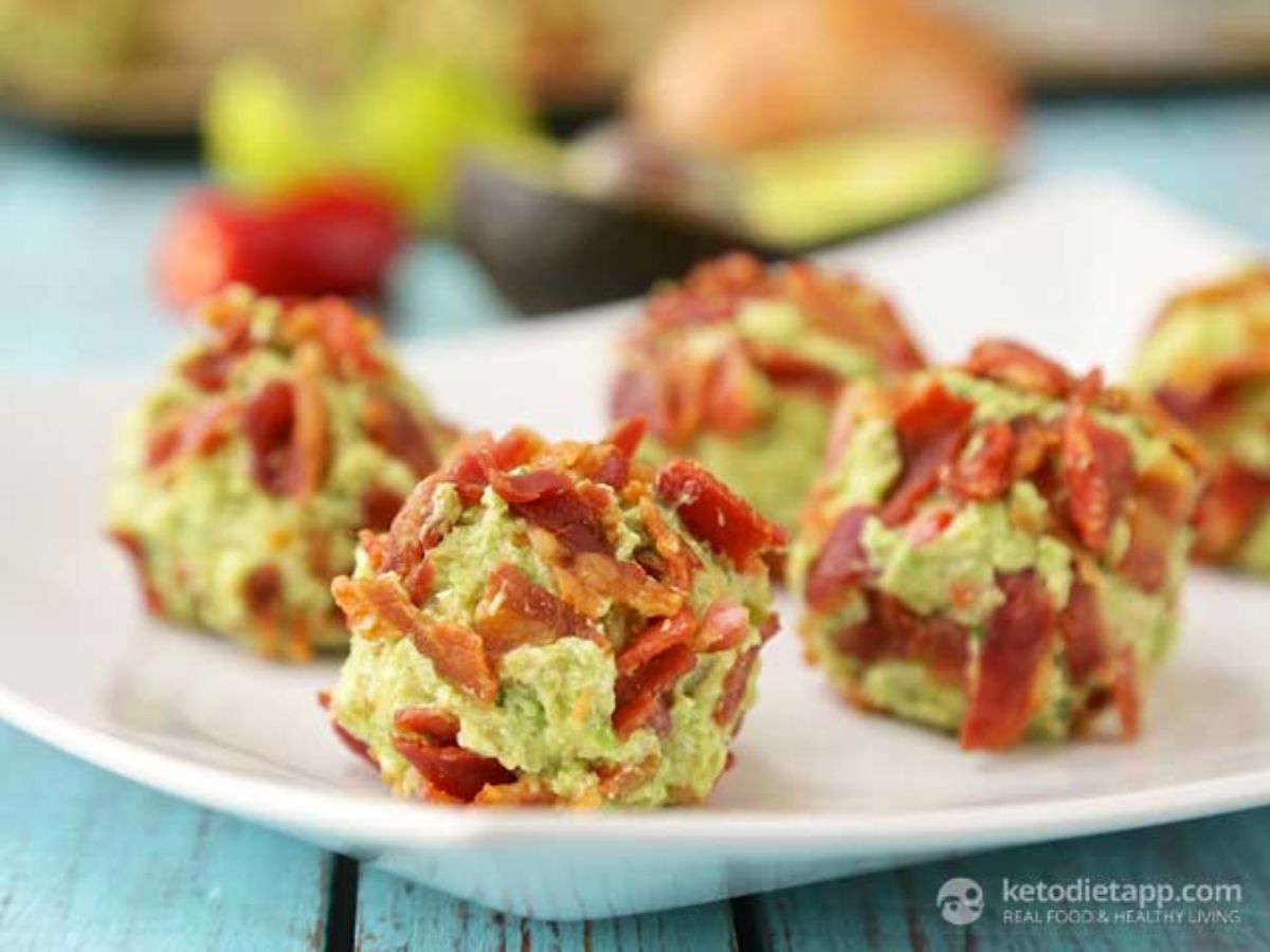 ON a bright blue wooden table is a square white plate holding 5 avocado balls encrusted with bacon bits