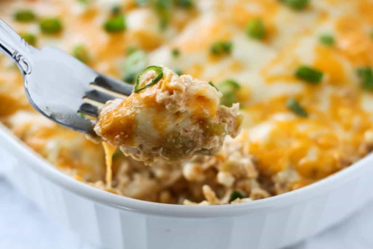 a blurred shot of a white ceramic dish with cheesey casserole adn chive garnsih. A metal fork lifts a portion out of the dish