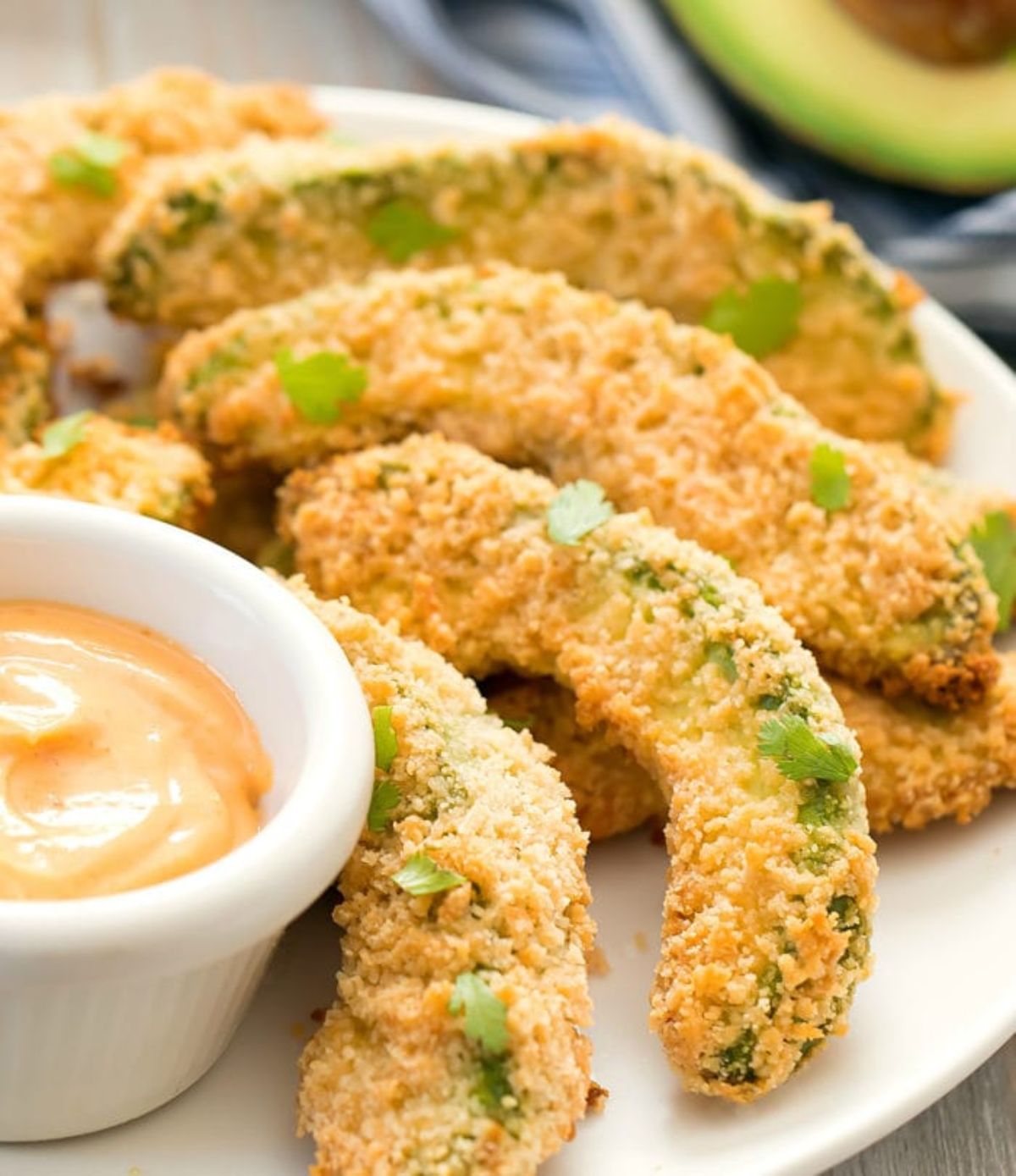 A partial shot of a white plate holding avocado fires and a white pot of sauce