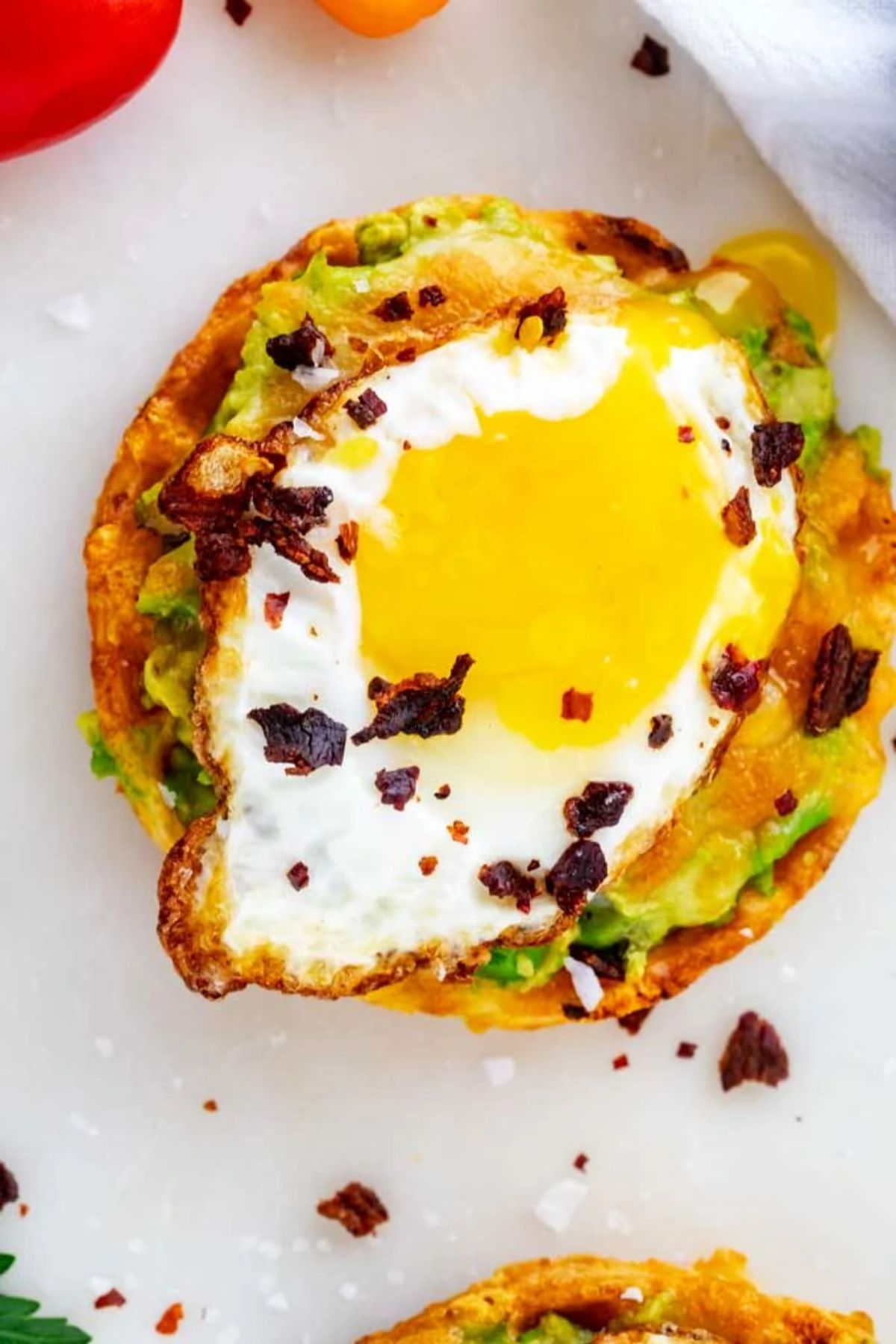 On a white background is a circular piece of avocado taost with a fried egg on top