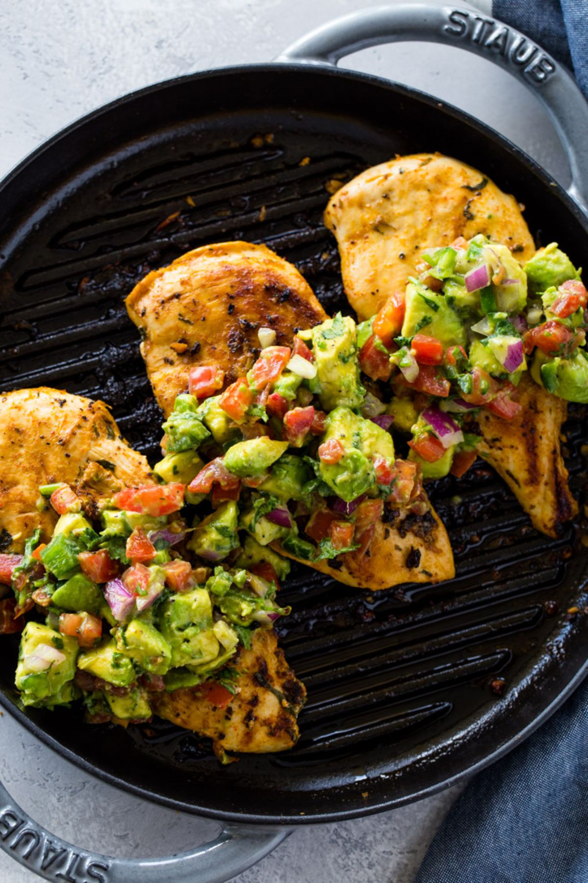 in a cast iron skillet are 3 cooked chicken breasts covered with avocado salsa