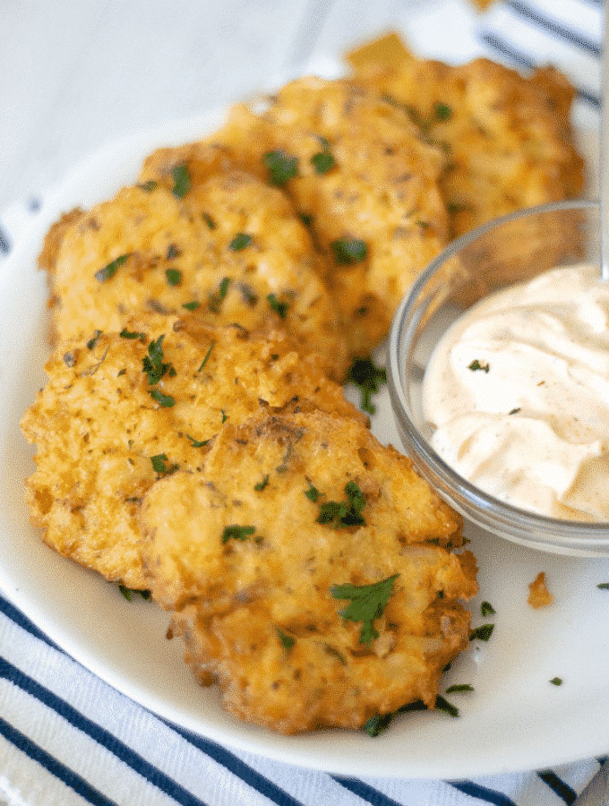 On a hwote plate are 5 small crab cakes, next to a glass bowl filled with white dip