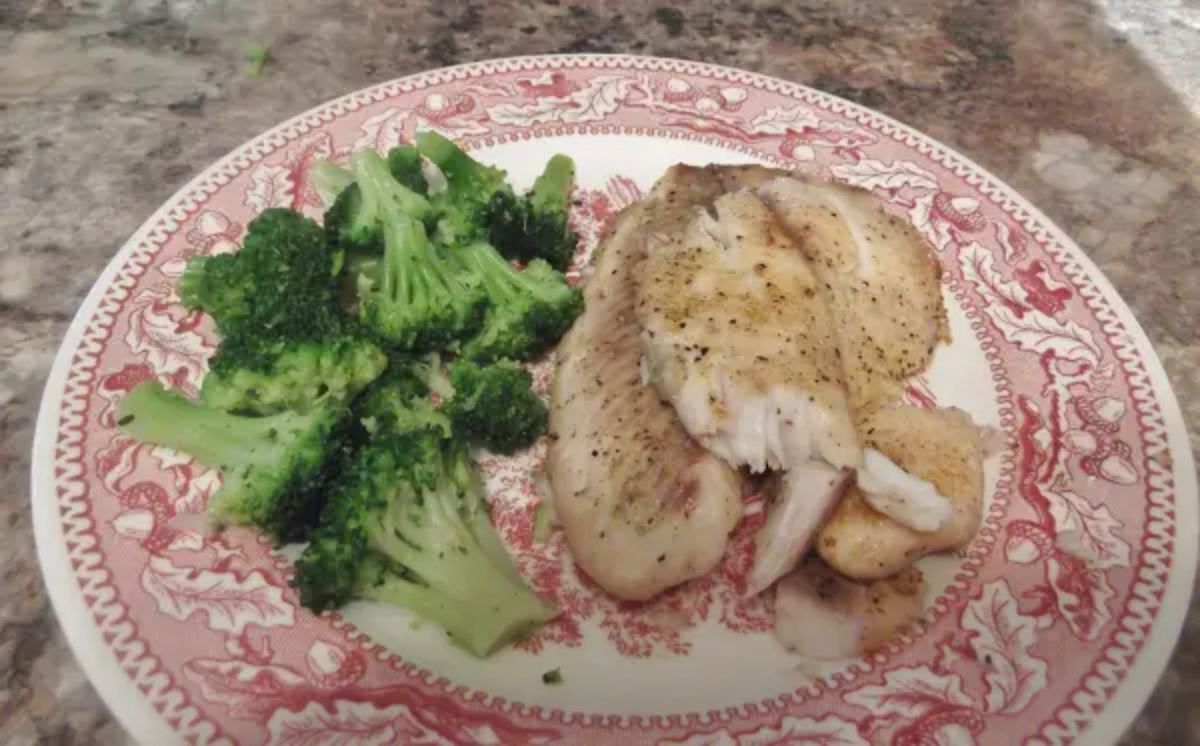 A red patterened plate holds a tilapia fillet and a pile of broccoli