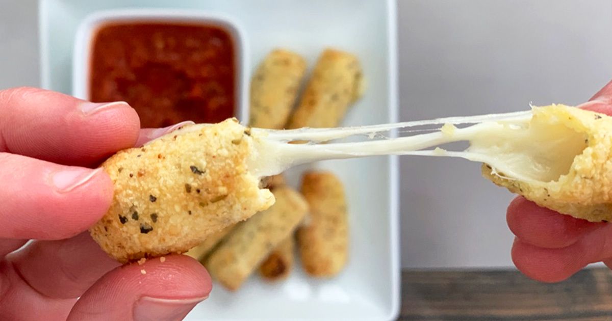 |Two hands pull apart a mozzarella stick. Behind them is a square white plate holding 5 mozzarella sticks and a bolw of red sauce