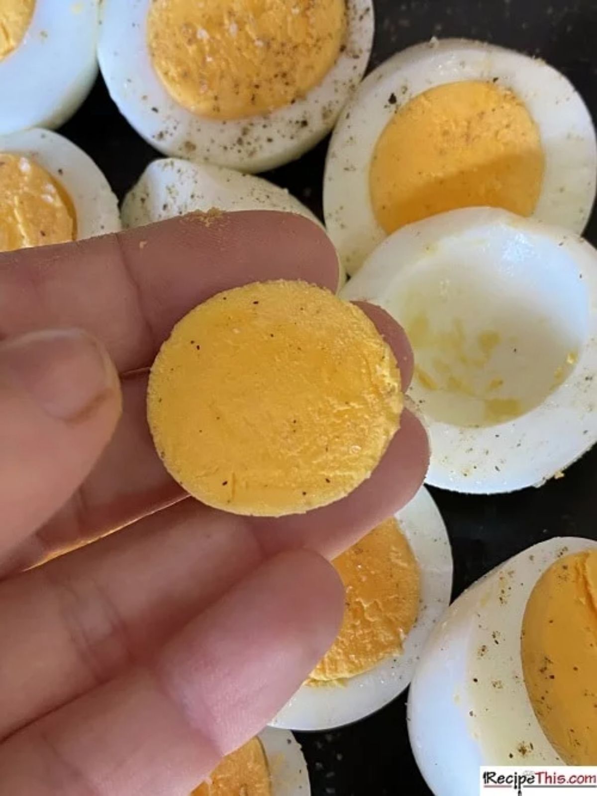 A hand picks the yolk of a hard boiled egg from a pile of halved hard boiled eggs