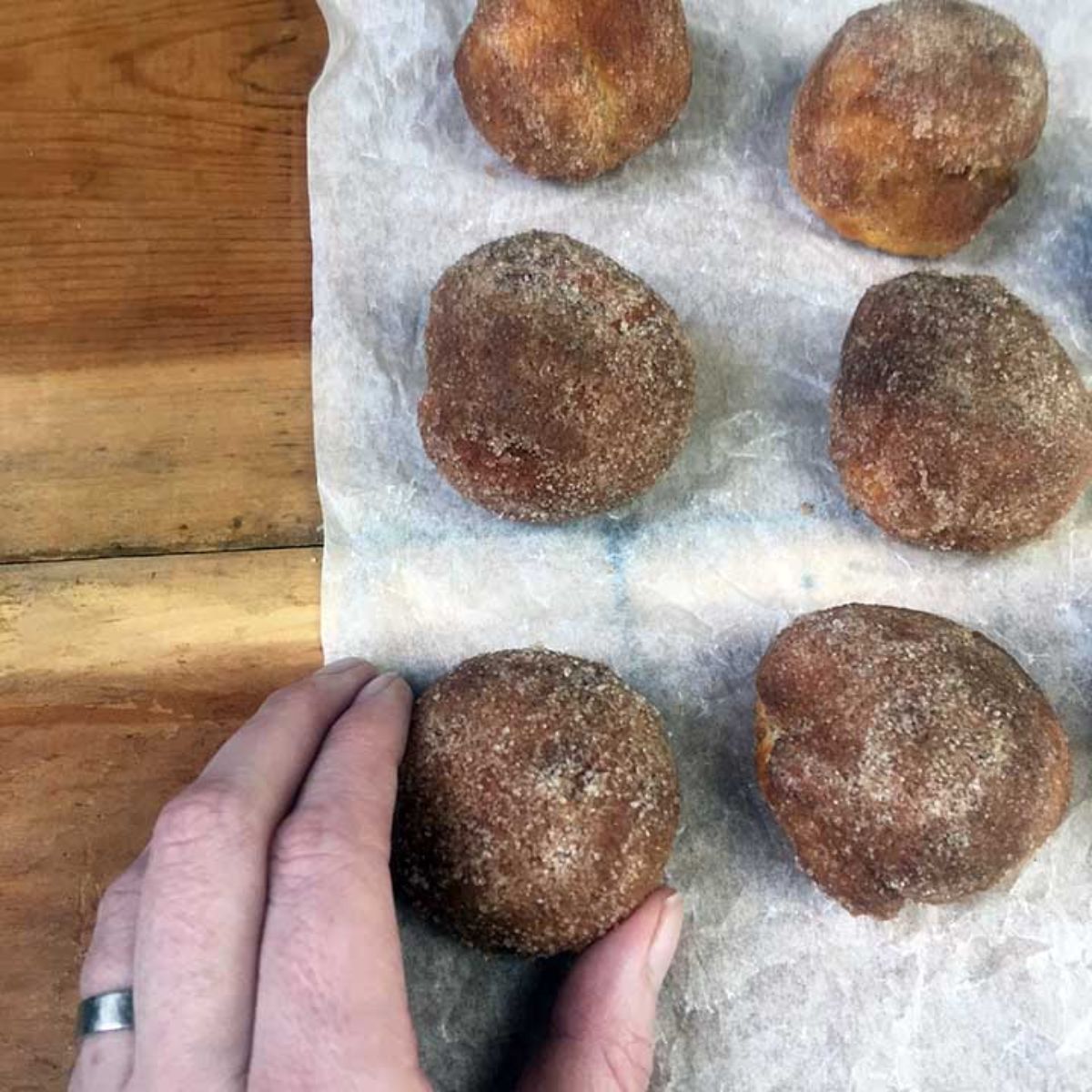 On a baking parchment are 6 donut holes with a hand holding the botto left one