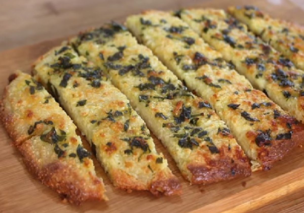 An oval flat loaf of garlic bread is cut into strips