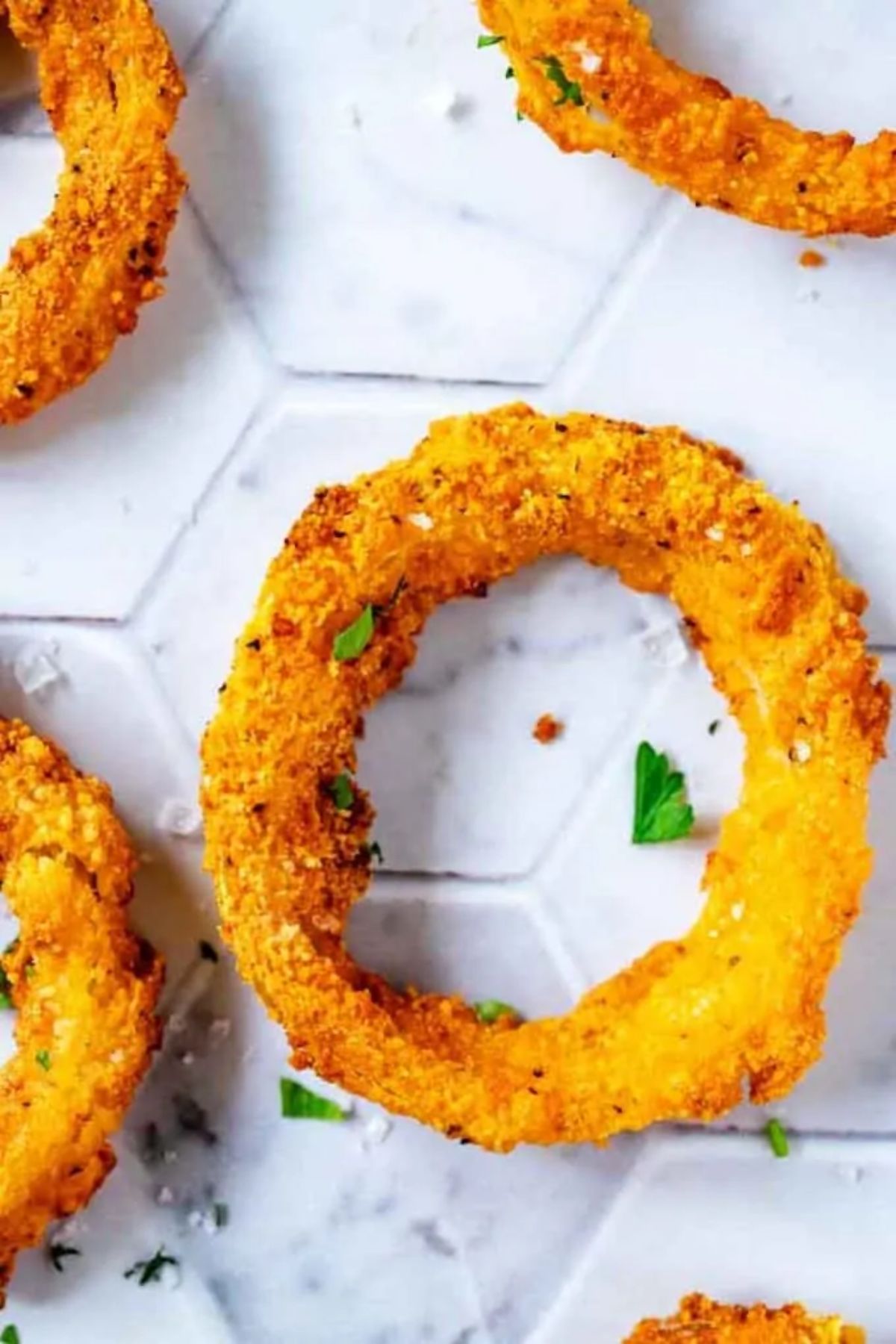 Ona white tiled surface are 4 breaded onion rings, sprinkled with sea salt and herbs