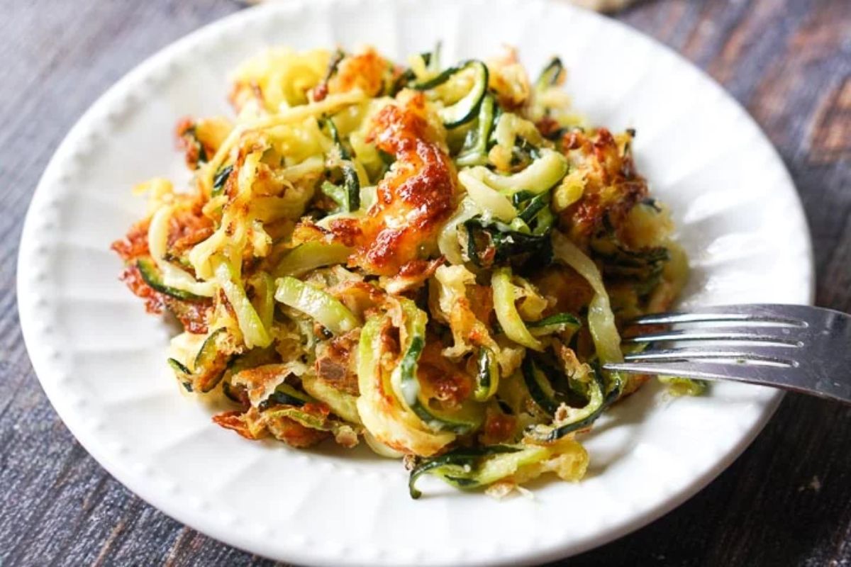 On a round white plate is a pile of zucchini noodles with a fork sticking into them
