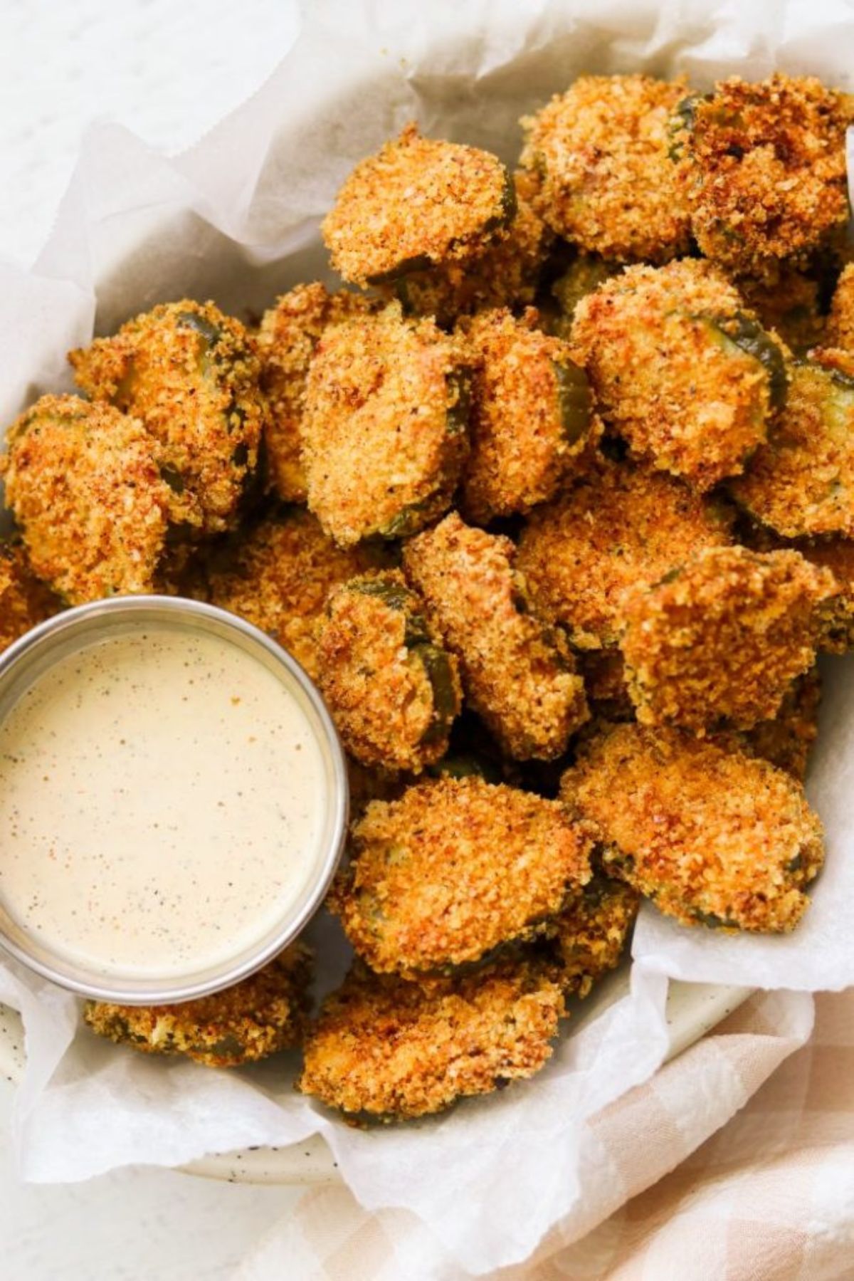 A parchment lined dish filled with fried pickles and a metal pot of a white dip