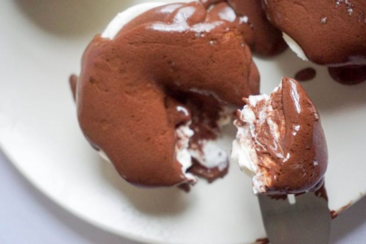 a to view of a small round cheesecake with a chocolate topping. A spoonfull has been cut out of it