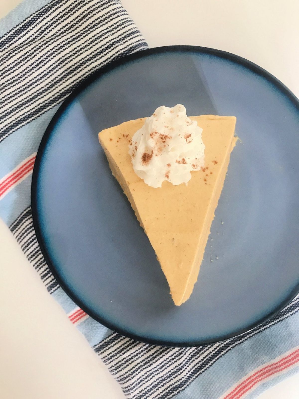 A top view of a blue plate with a vanilla cheesecake slice on it, topped with a swirl of cream