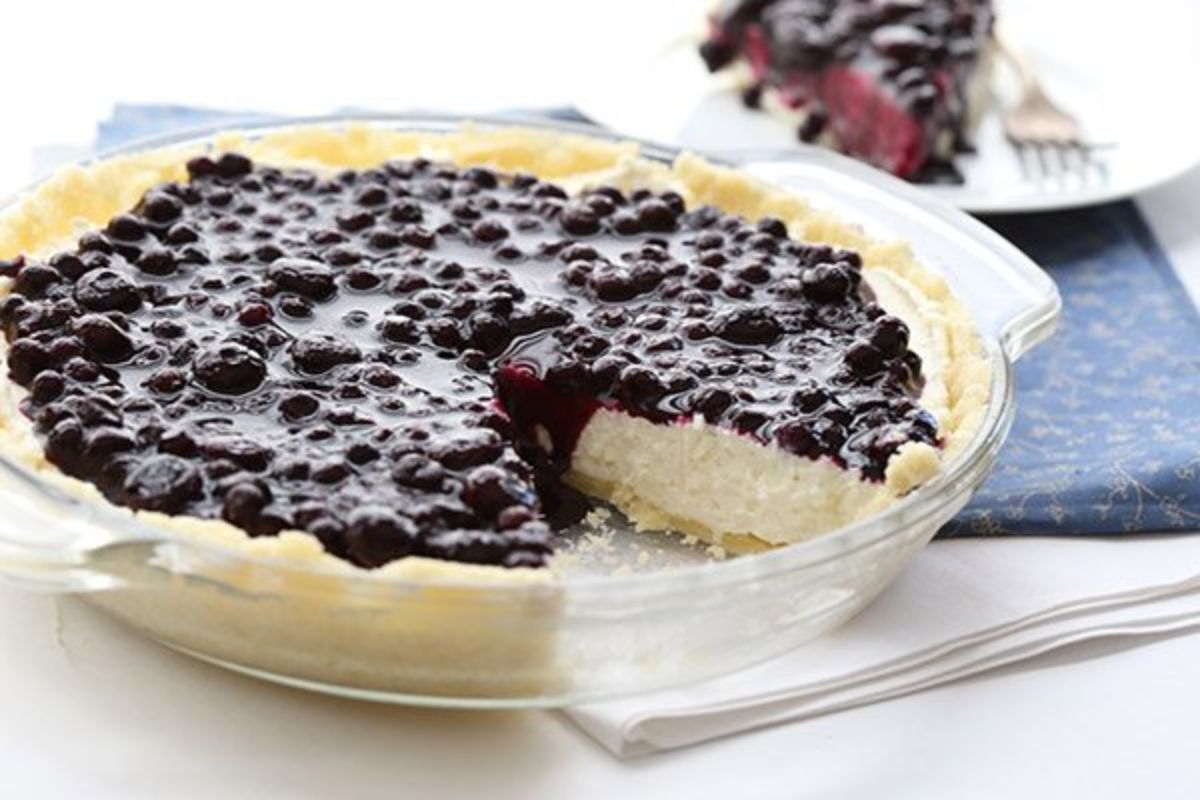 In a glass pie dish is a cheesecake covered in blueberry coulis, with a slice missing