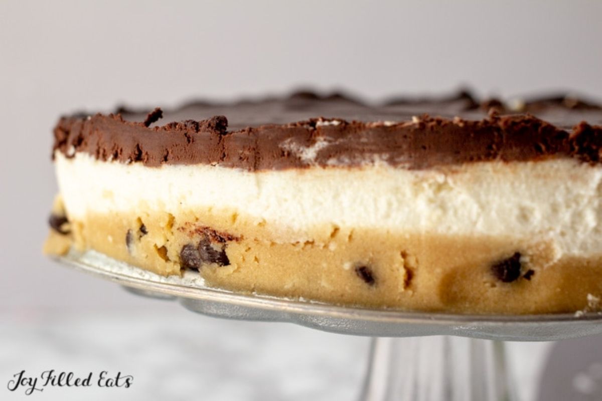 A section of a 3 layered cheesecake: biscut, cream and chocolate on a glass cake stand
