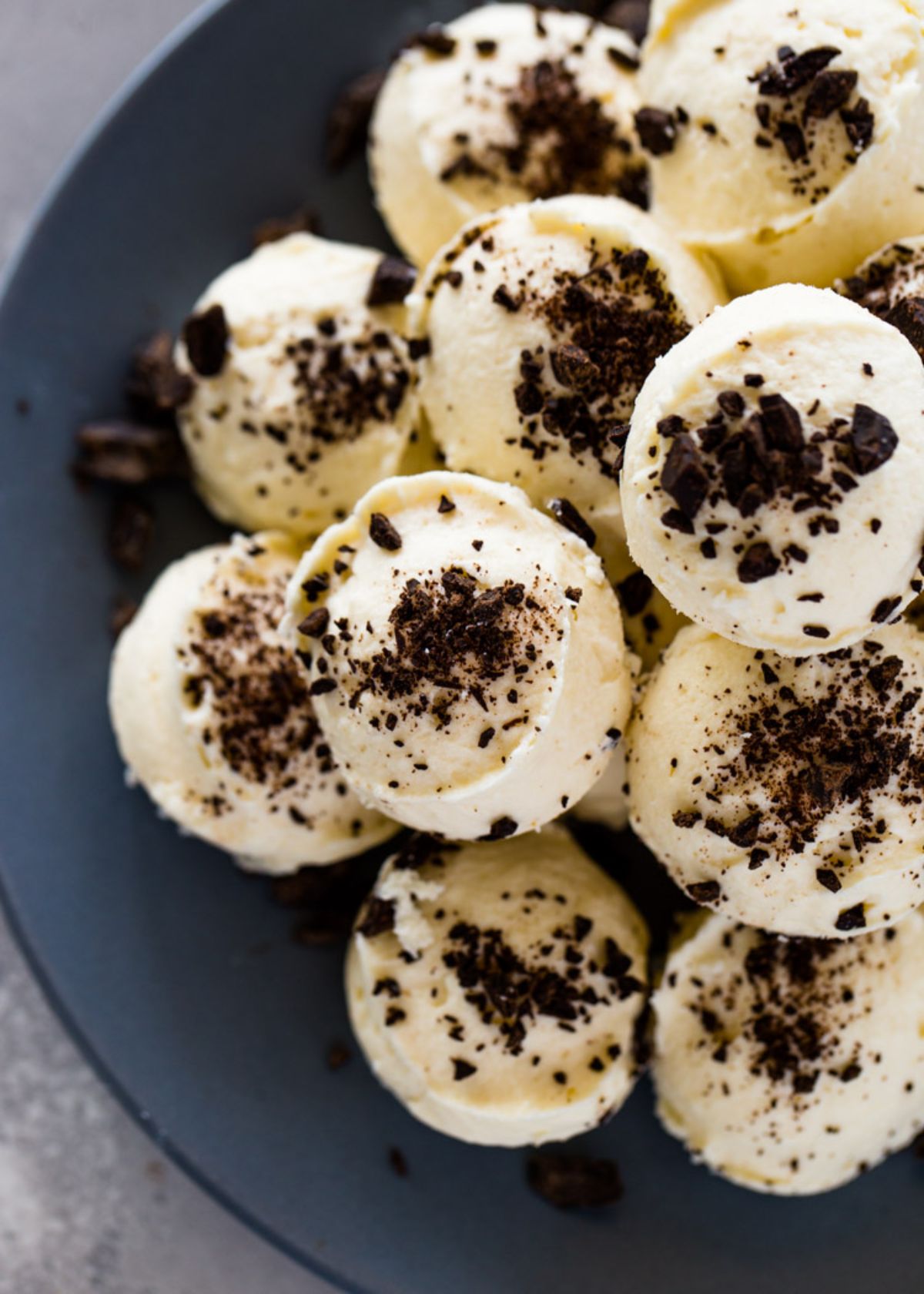 A gray plate with a pile of crea, coored cheesecake balls sprinkled with cocoa powder