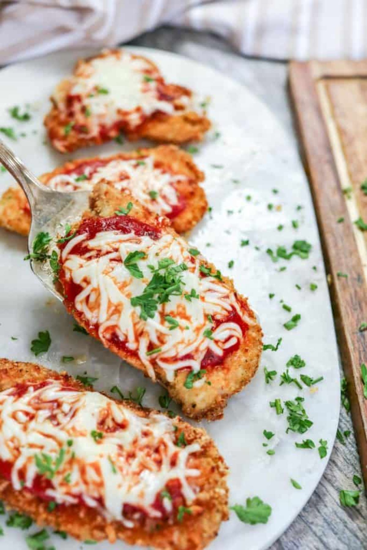On a white oval platter are 4 chicken parmesan portions, scattered with chopped herbs
