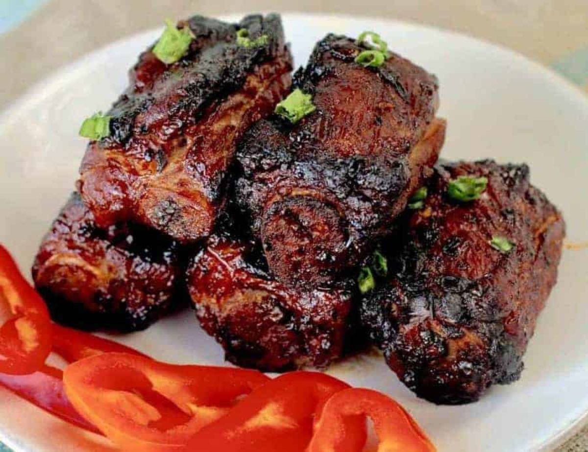 5 spare ribs are on a white plate, with sliced red pepper in front of them