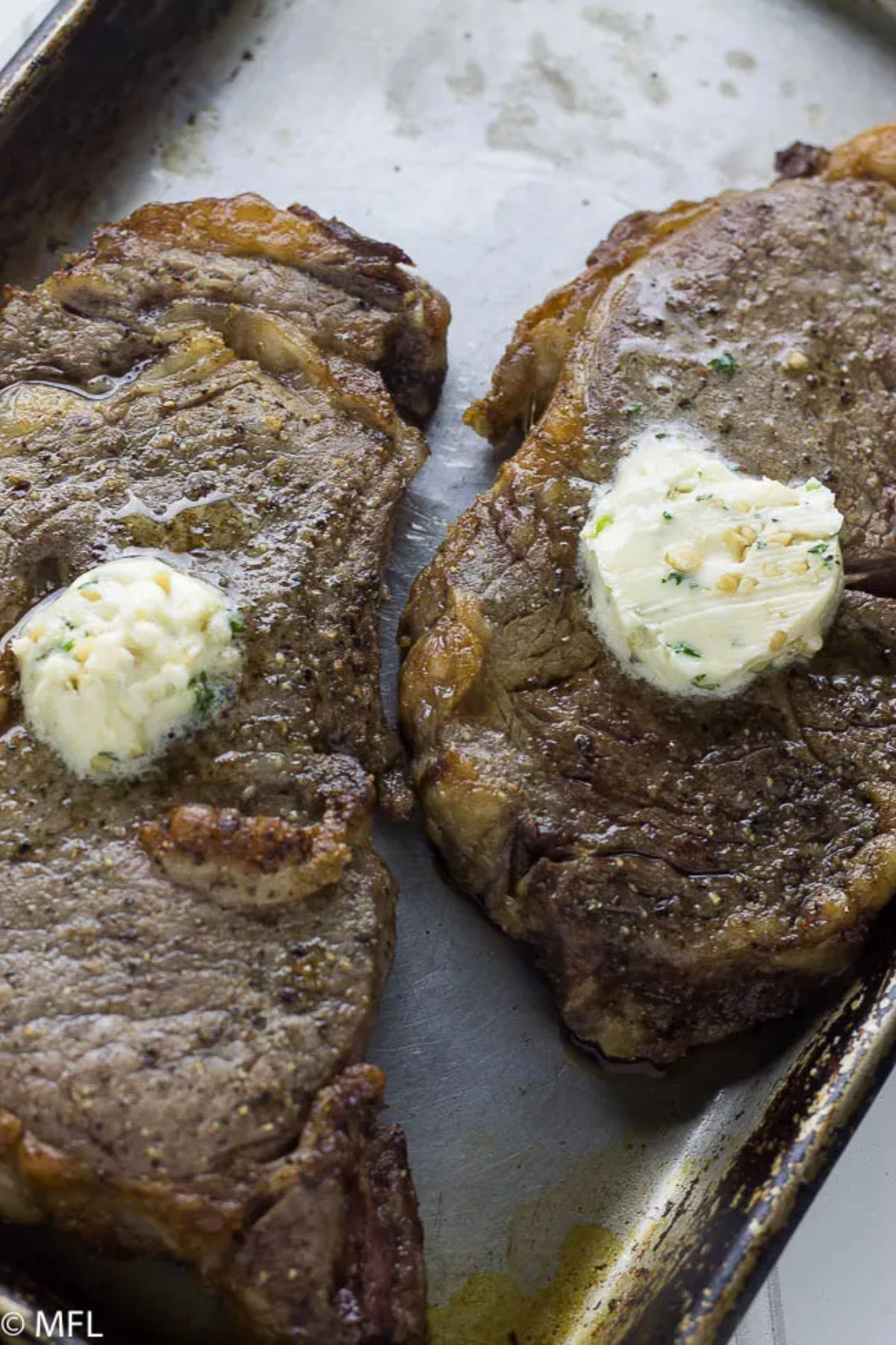 A roasting tray holds 2 cooked steaks topped with herbed butter