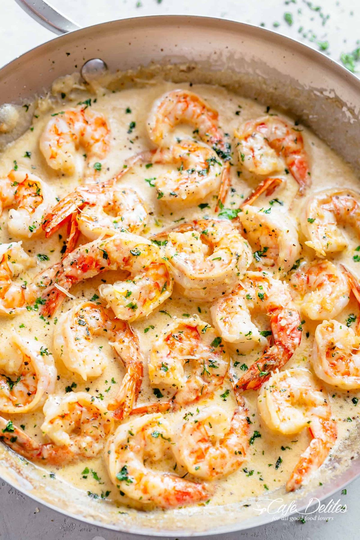 om a white surface is a skillet fill of prawns in a creamy sauce, sprinkled with green herbs