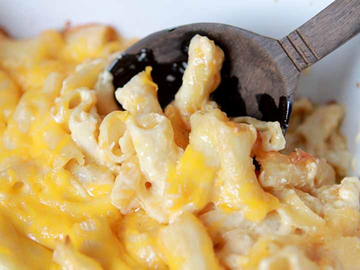 a partial shot of a bowl of macaroni and cheese with a wooden sppon scooping some out of the bowl