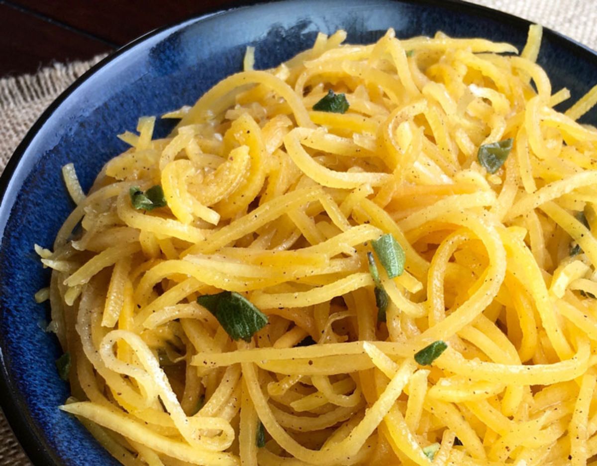 in a dark blue bowl is a pile of spaghetti with chopped basil garnish