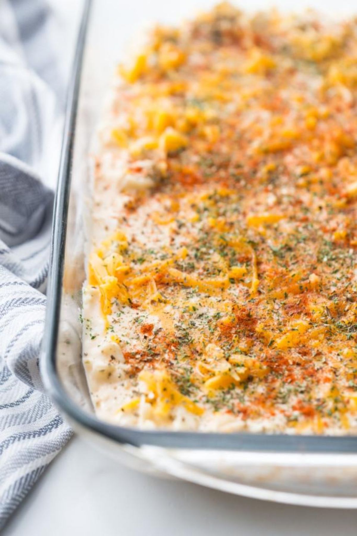 a section of a glass dish with creamy casserole and cheese sprinkled on top