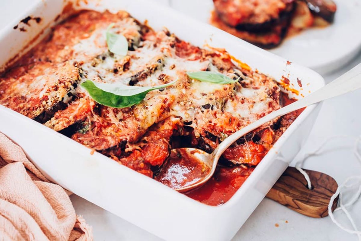 ON a wooden chopping board is a rectangle casserole dish filled with layers of aubergine tomatoe sauce and cheese