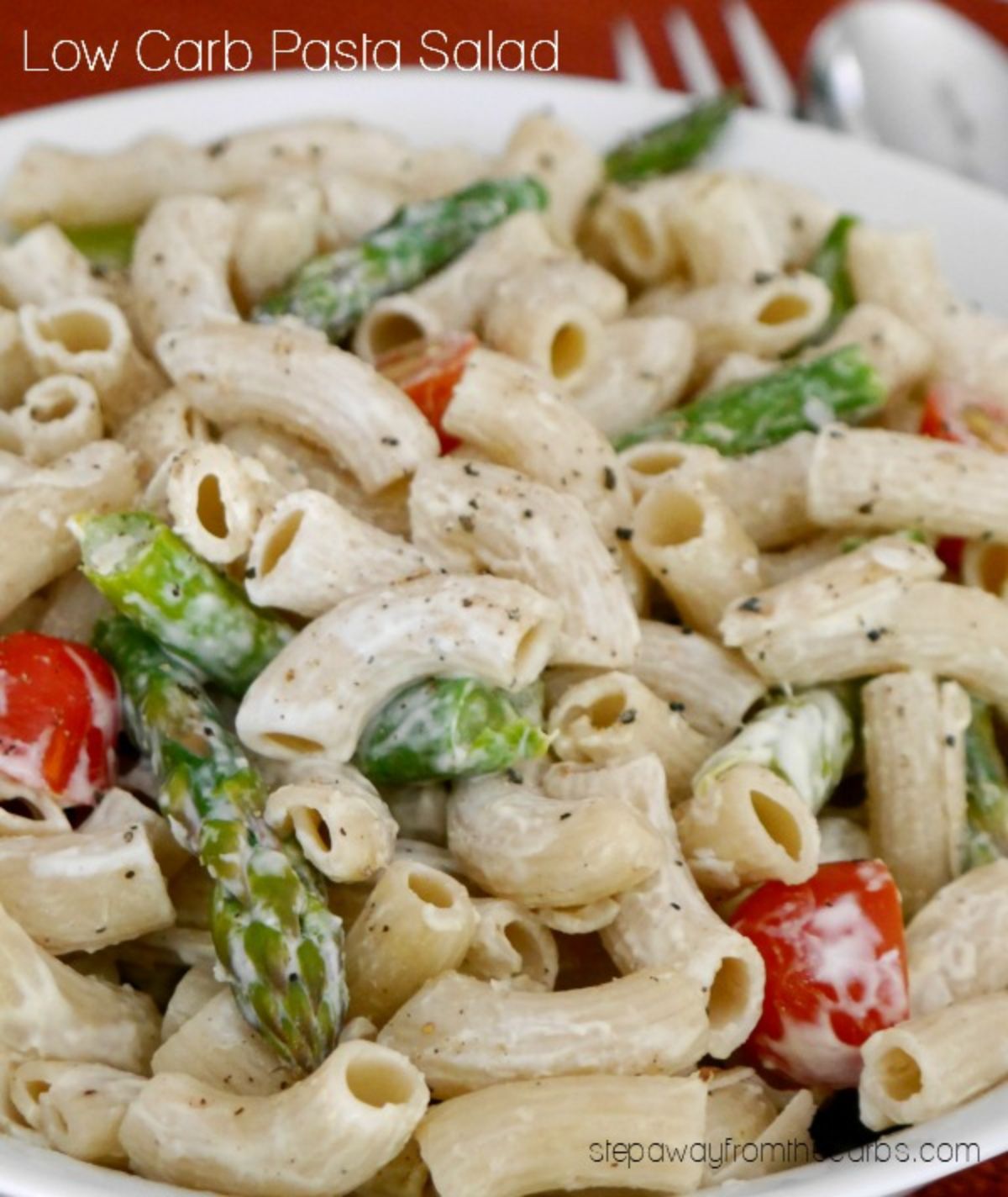 The text reads "Low Carb Pasta Salad". A white bowl is filled with tube pasta mixed with a creamy sauce, green beans and halved cherry tomatoes