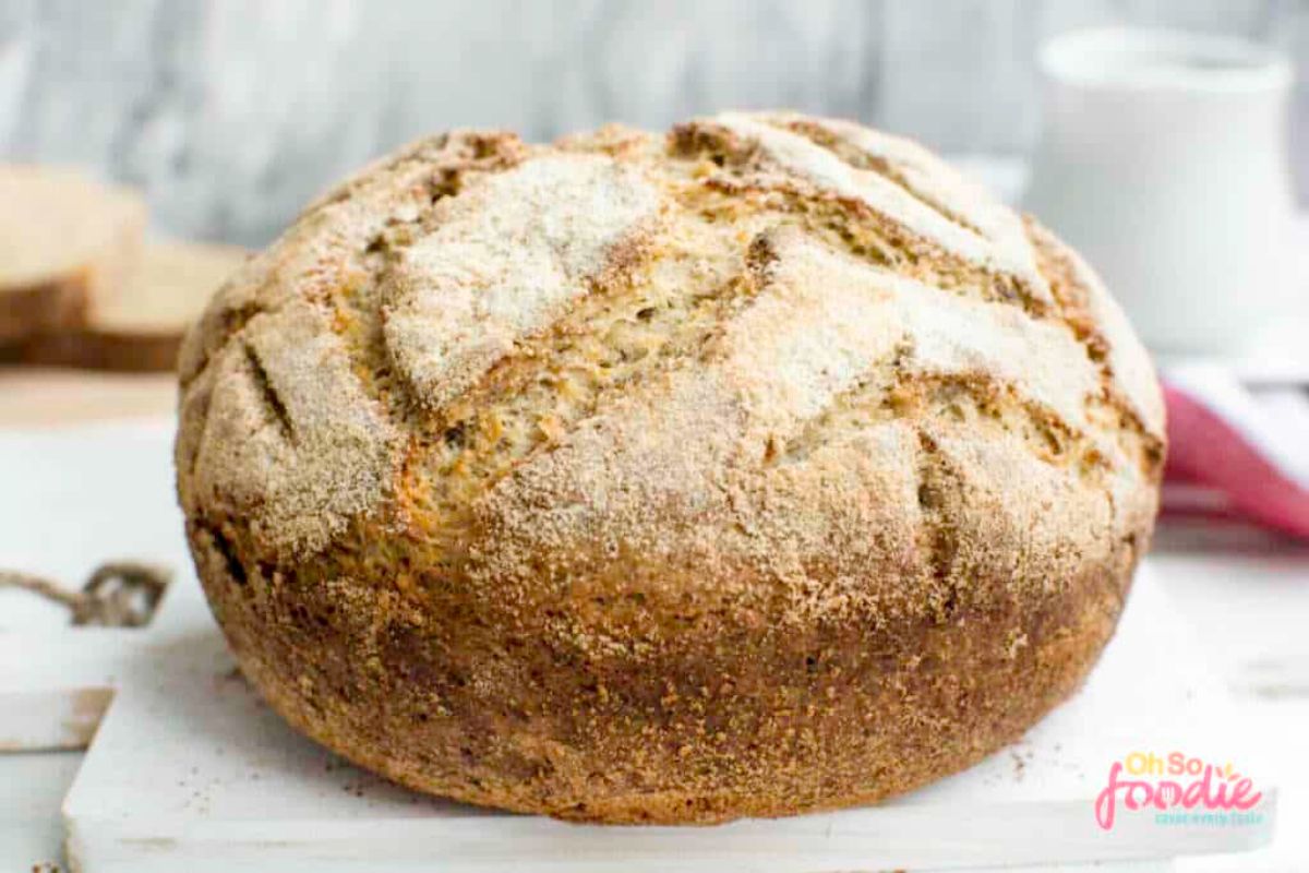 On a stone board is a round loaf of bread with a cracked top and sprinkled with flour