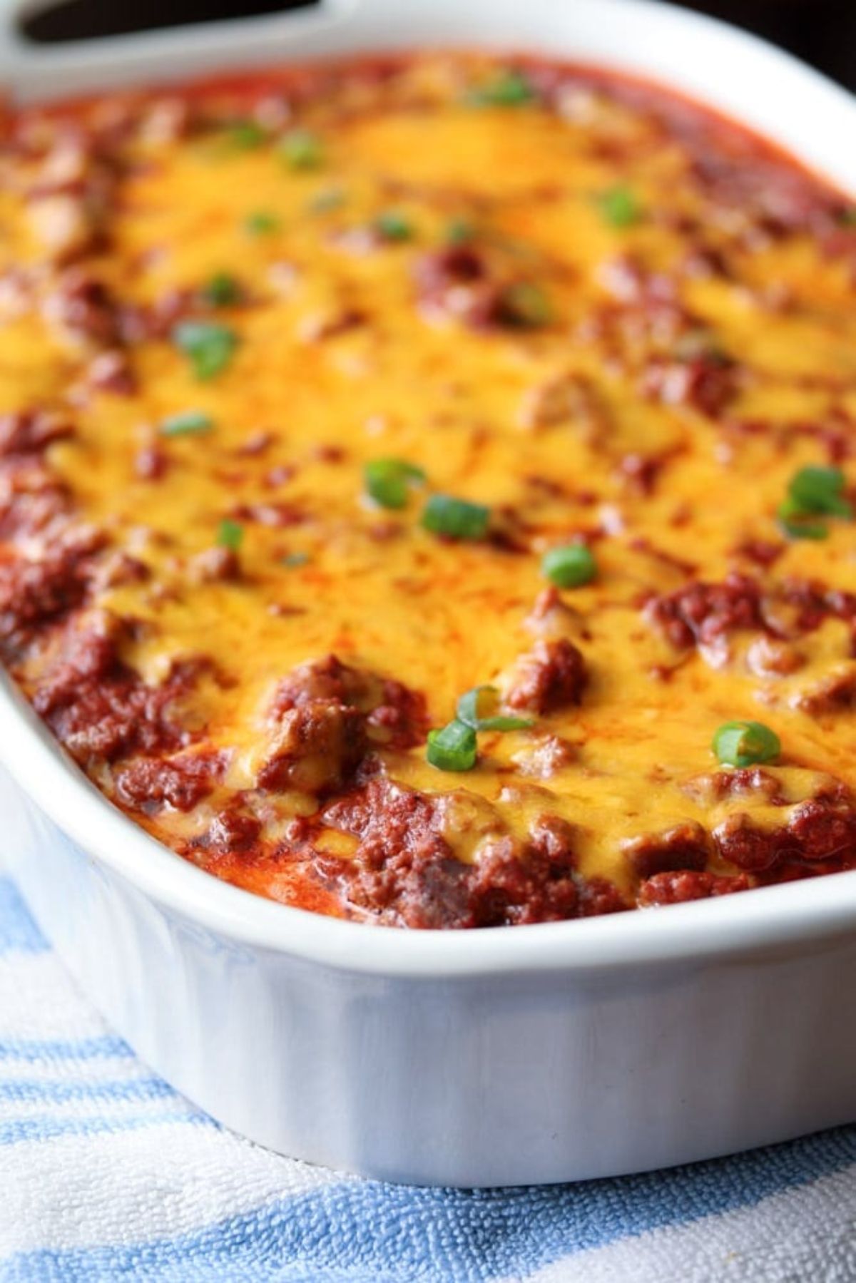 a slightly blurred photo of a white dish of a meaty and cheesy casserole with chive garnish